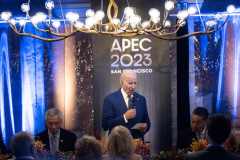 Joe Biden speaks to a group of people in a crowded room with signage &quot;APEC 2023&quot; in the background