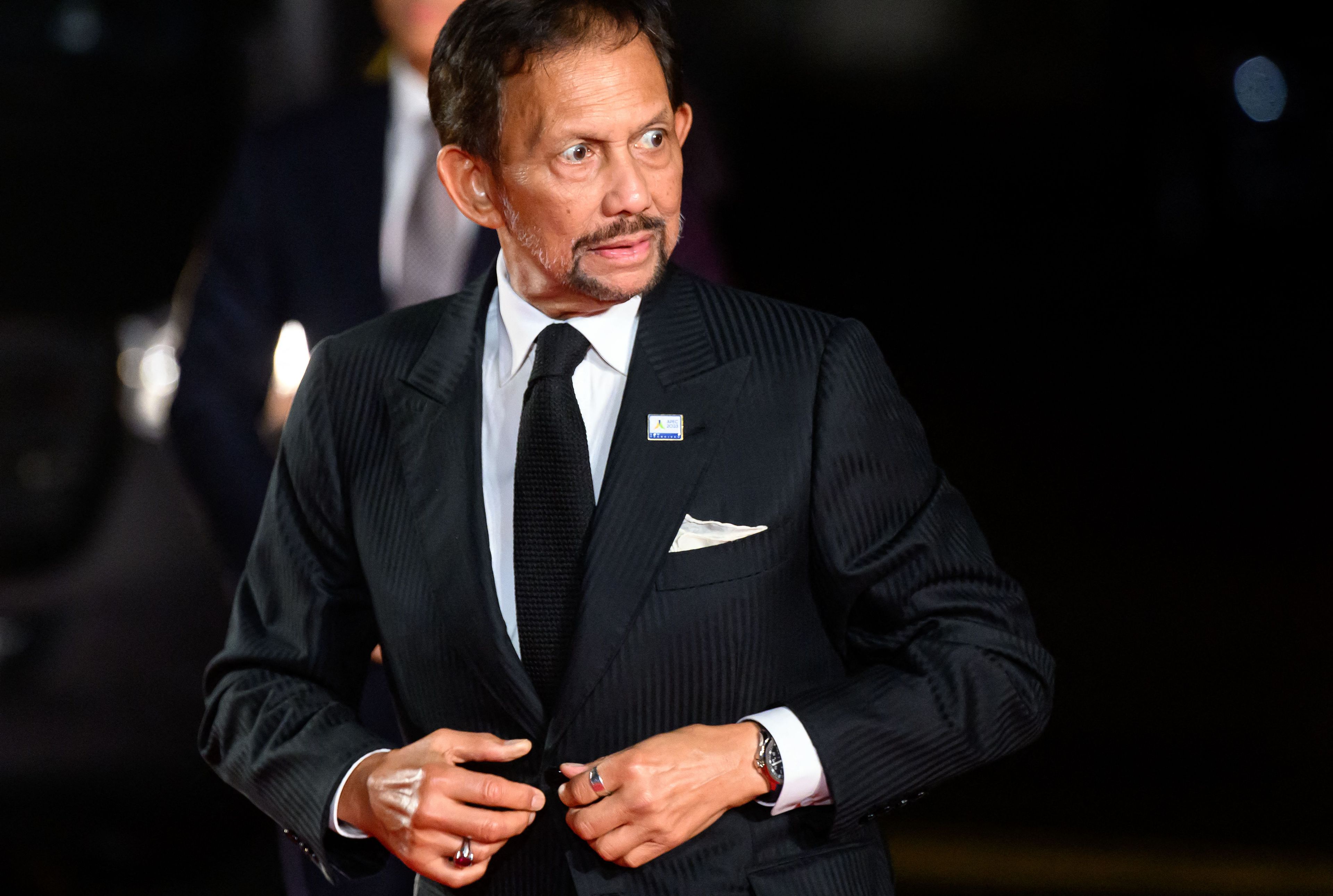 Brunei's Sultan Hassanal Bolkiah buttons up his suit while looking off camera.