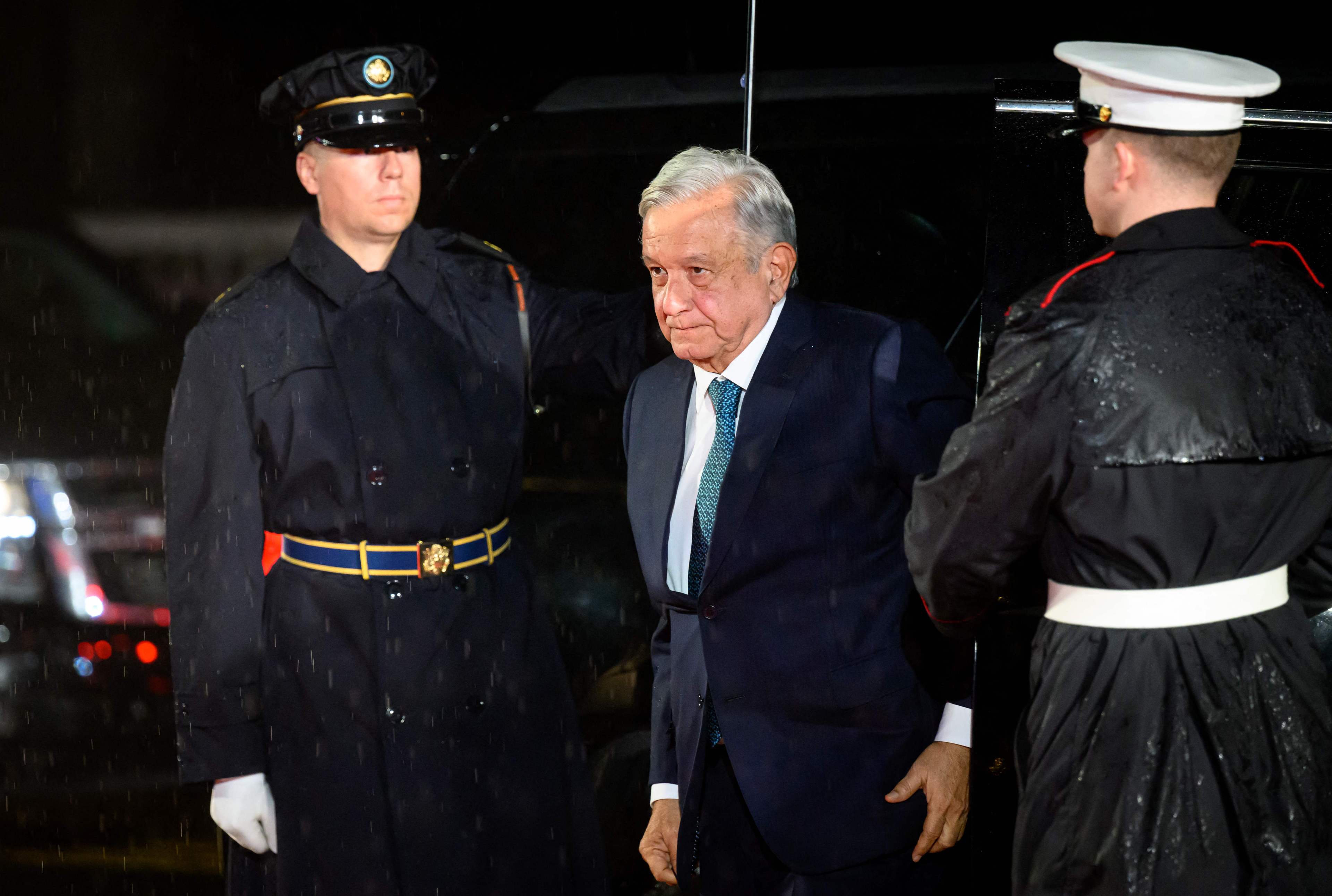 Mexico's President Andres Manuel Lopez Obrador, dressed in a suit walks between two members of security personnel.