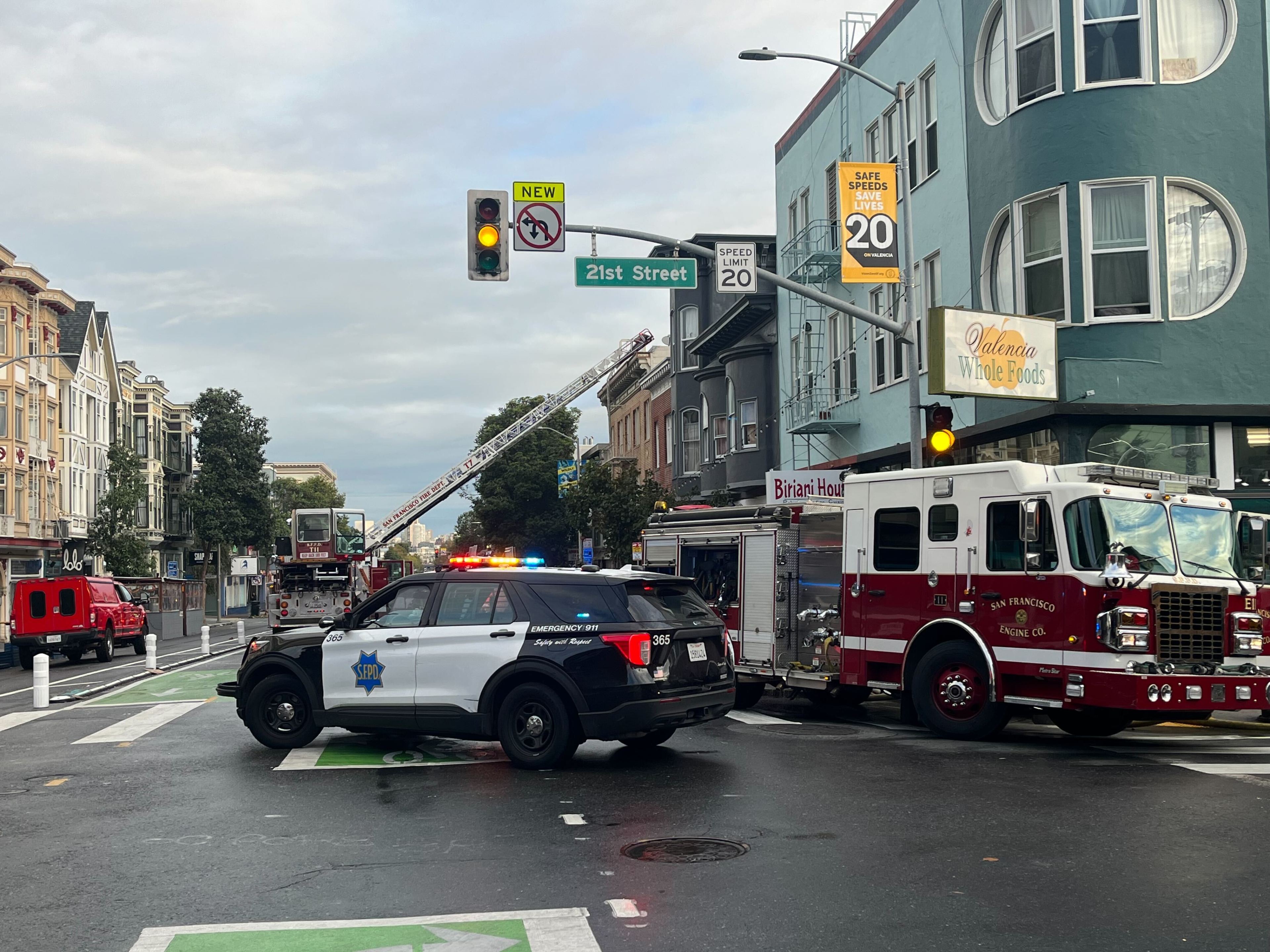 A police sport-utility vehicle blocks traffic at an intersection while a fire engine and hook and ladder truck work to contain a fire.