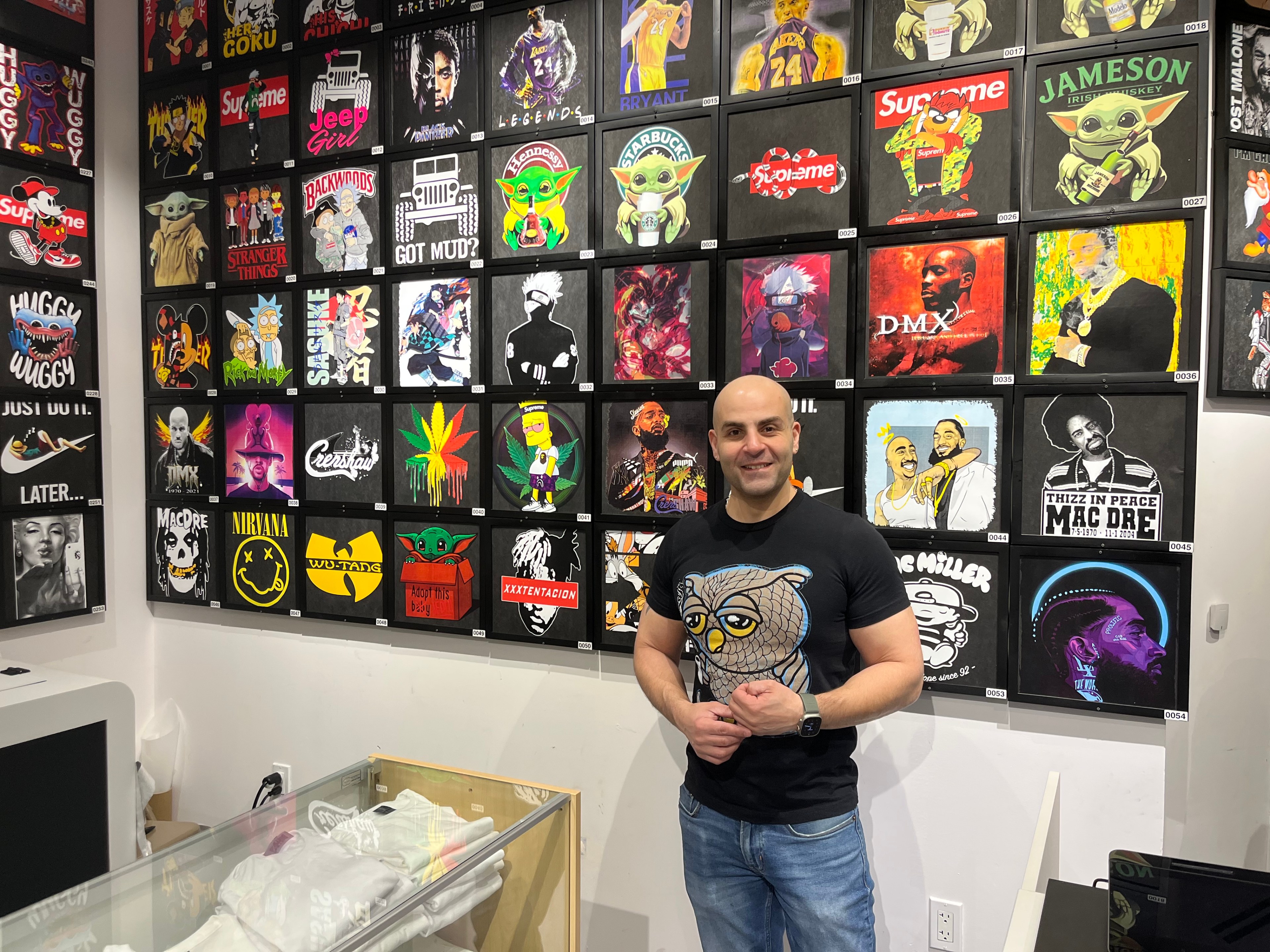 Customania owner, Shoka, stands in front of a wall of customed T-shirts at his store in San Francisco on Monday.