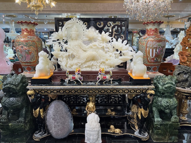 A jade Buddha statue sits on an antique desk surrounded by fine art objects.