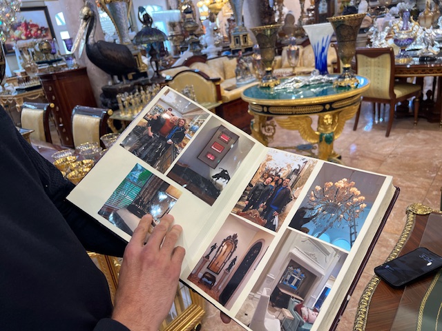 A man holds a photo album in his hands that have pictures of people and fine art objects.