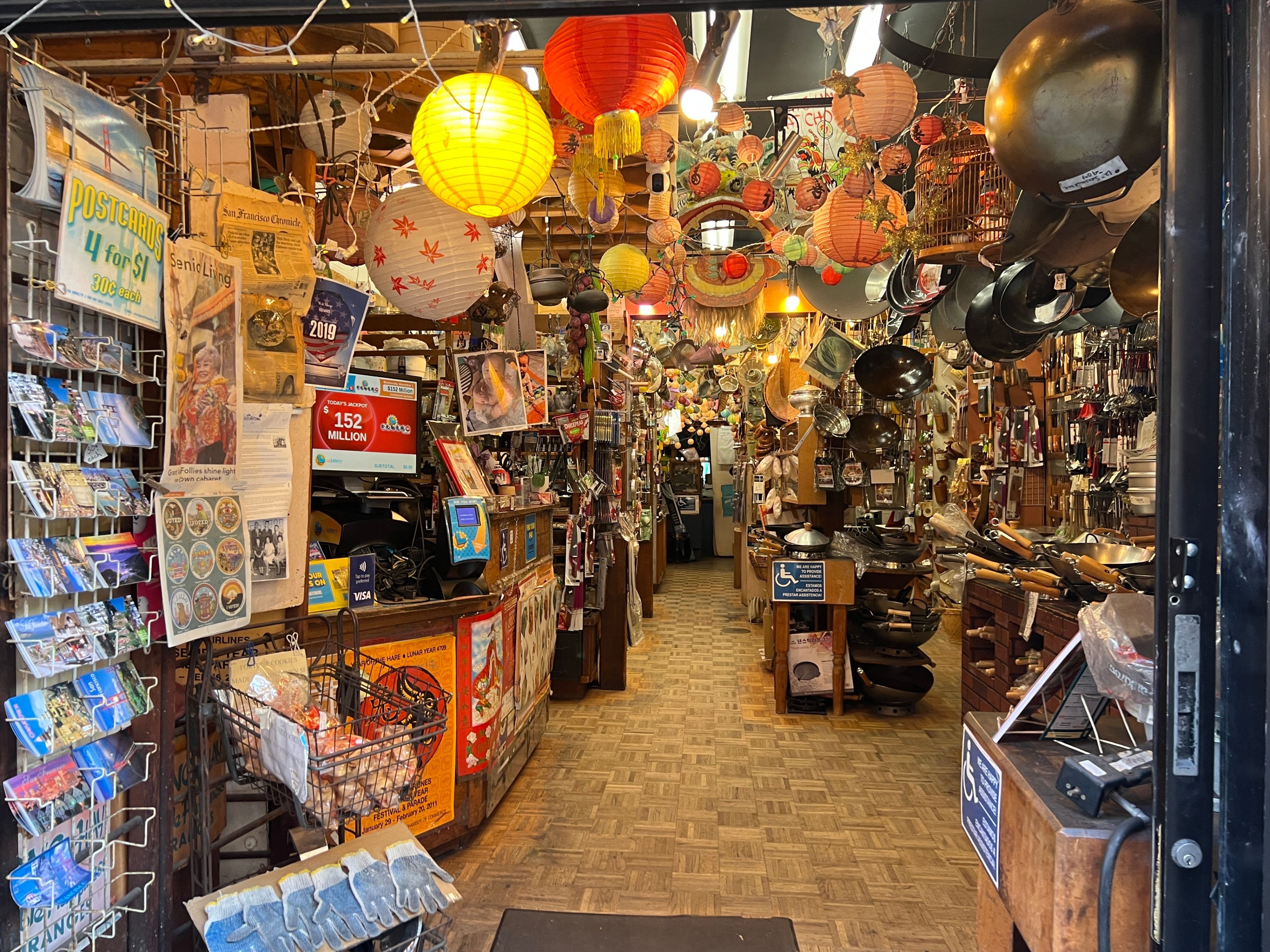 The entrance to a store shows hanging woks and pans, kitchen tools, postcards and paper lanterns.