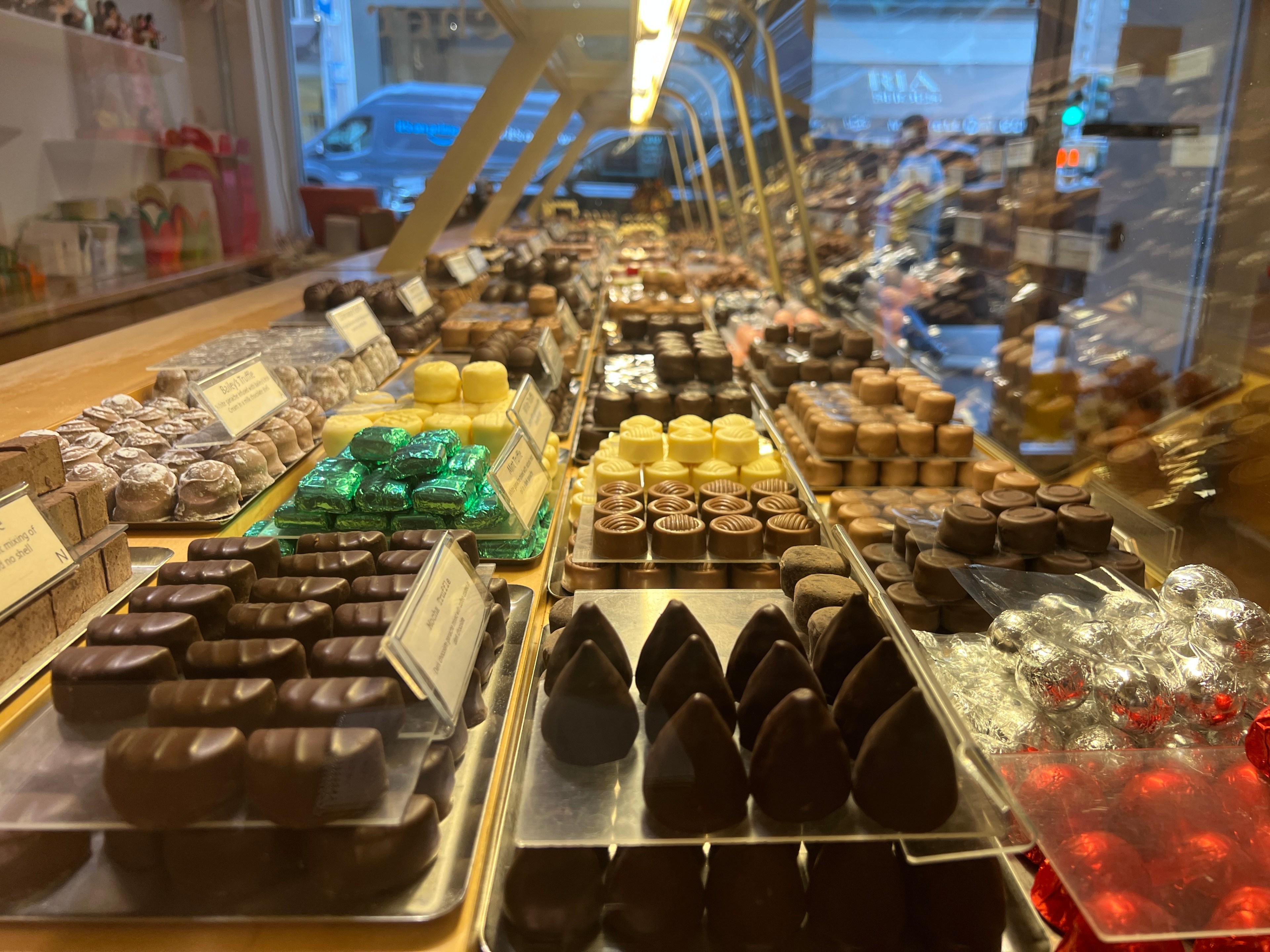 An assortment of individual chocolates is visible through a glass display case.