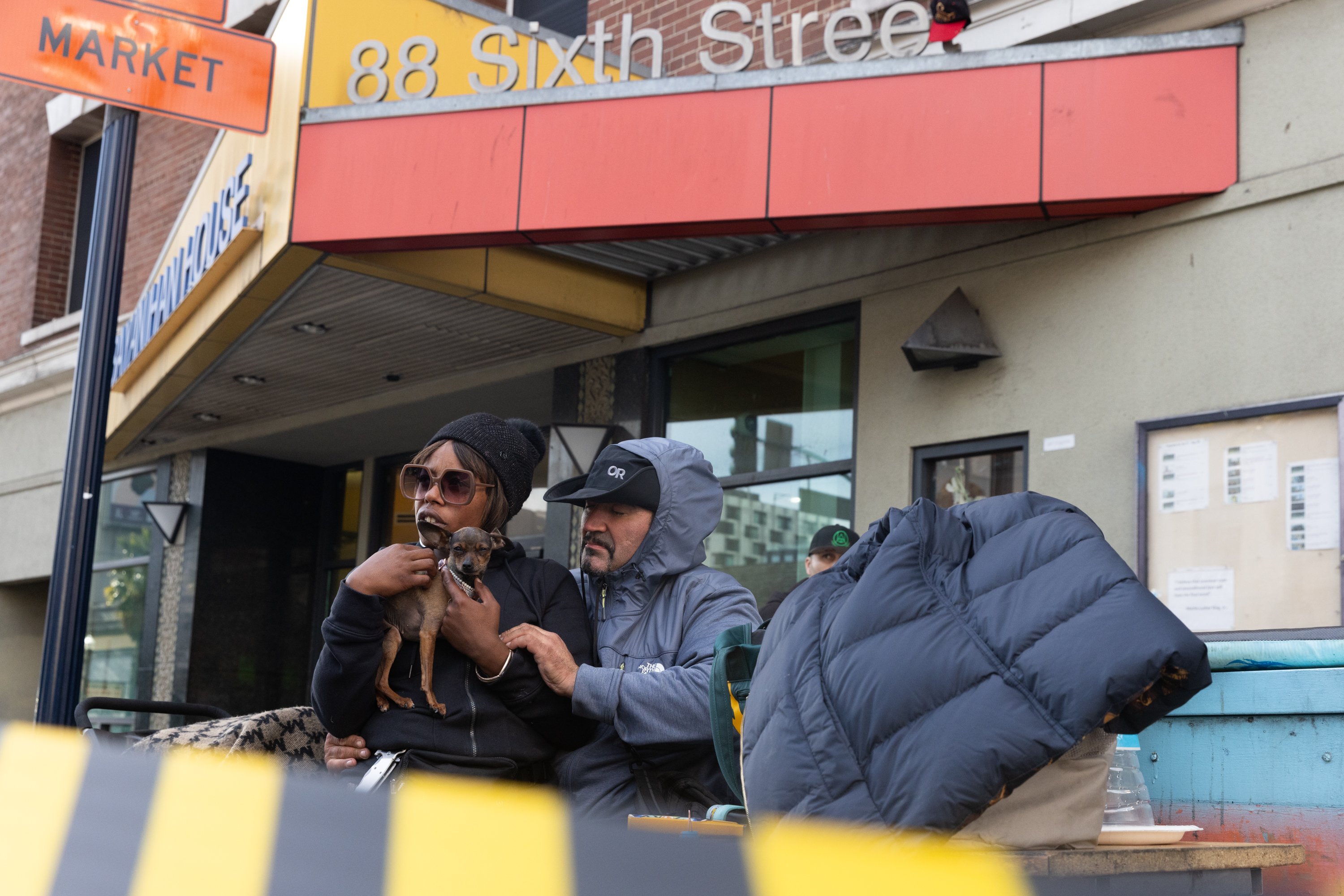 A woman holding a dog sits on a man's lap on sixth street.