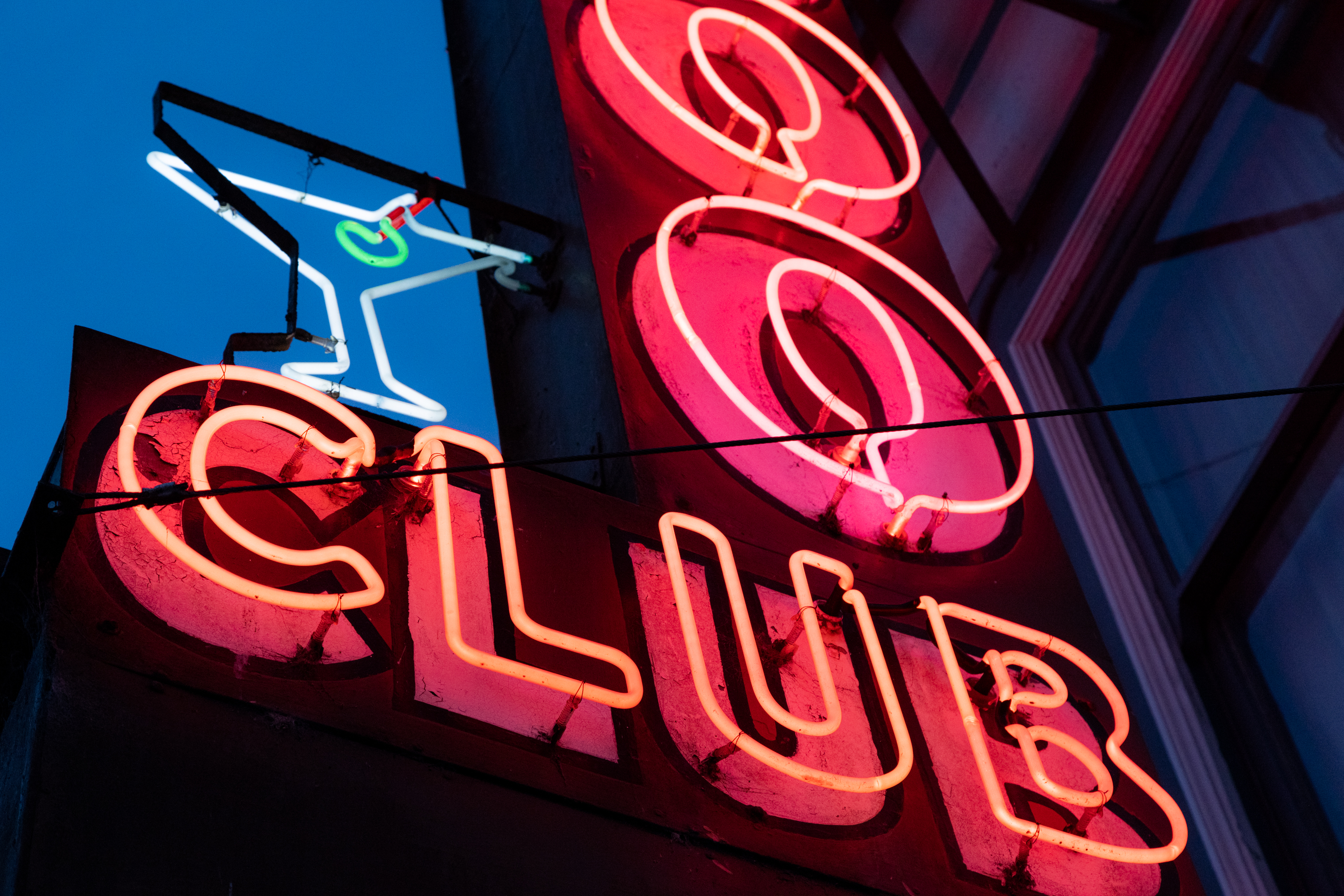 A neon sign at night that reads Club with a detail of a cocktail