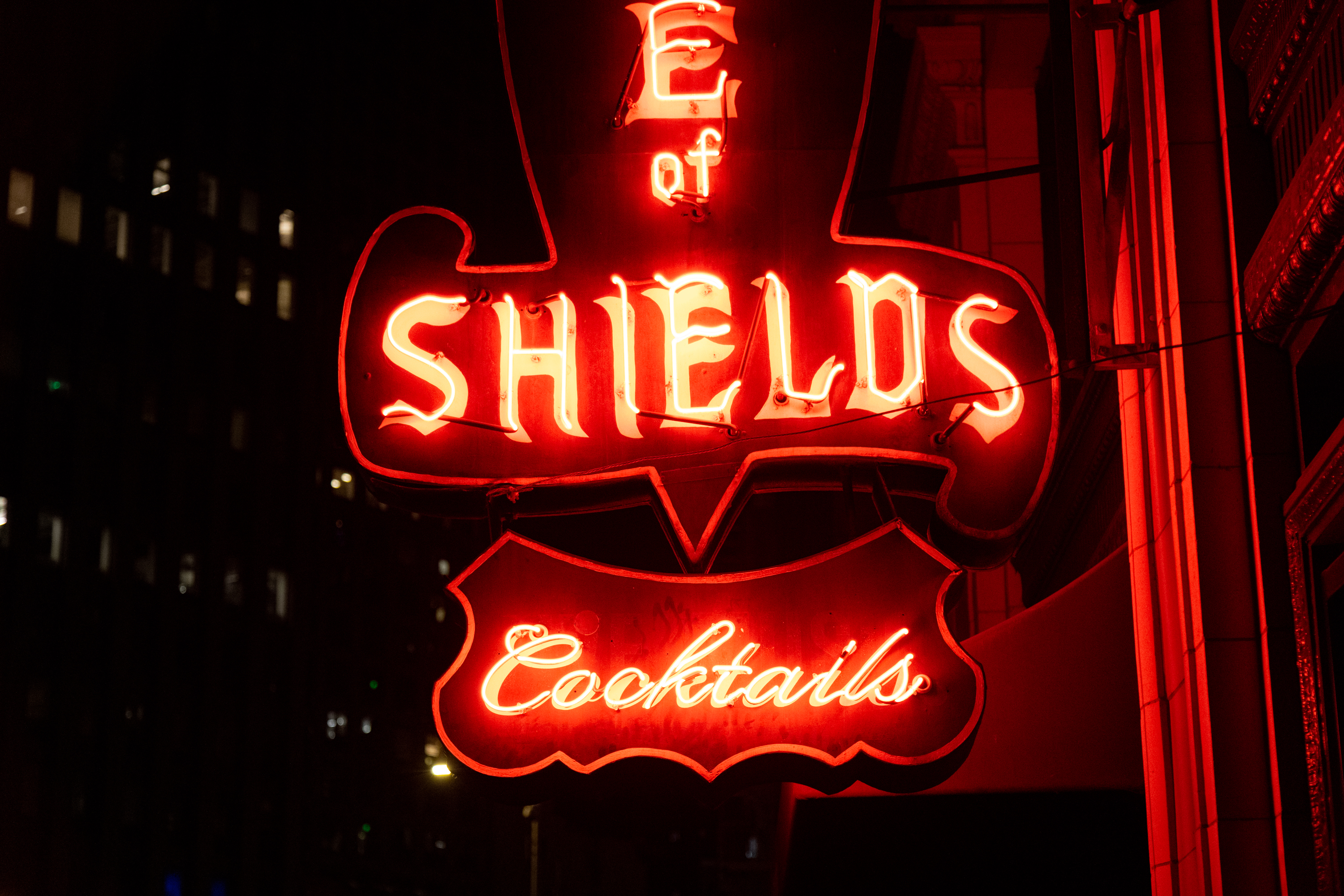 A red neon sign at night that reads &quot;SHIELDS Cocktails&quot;