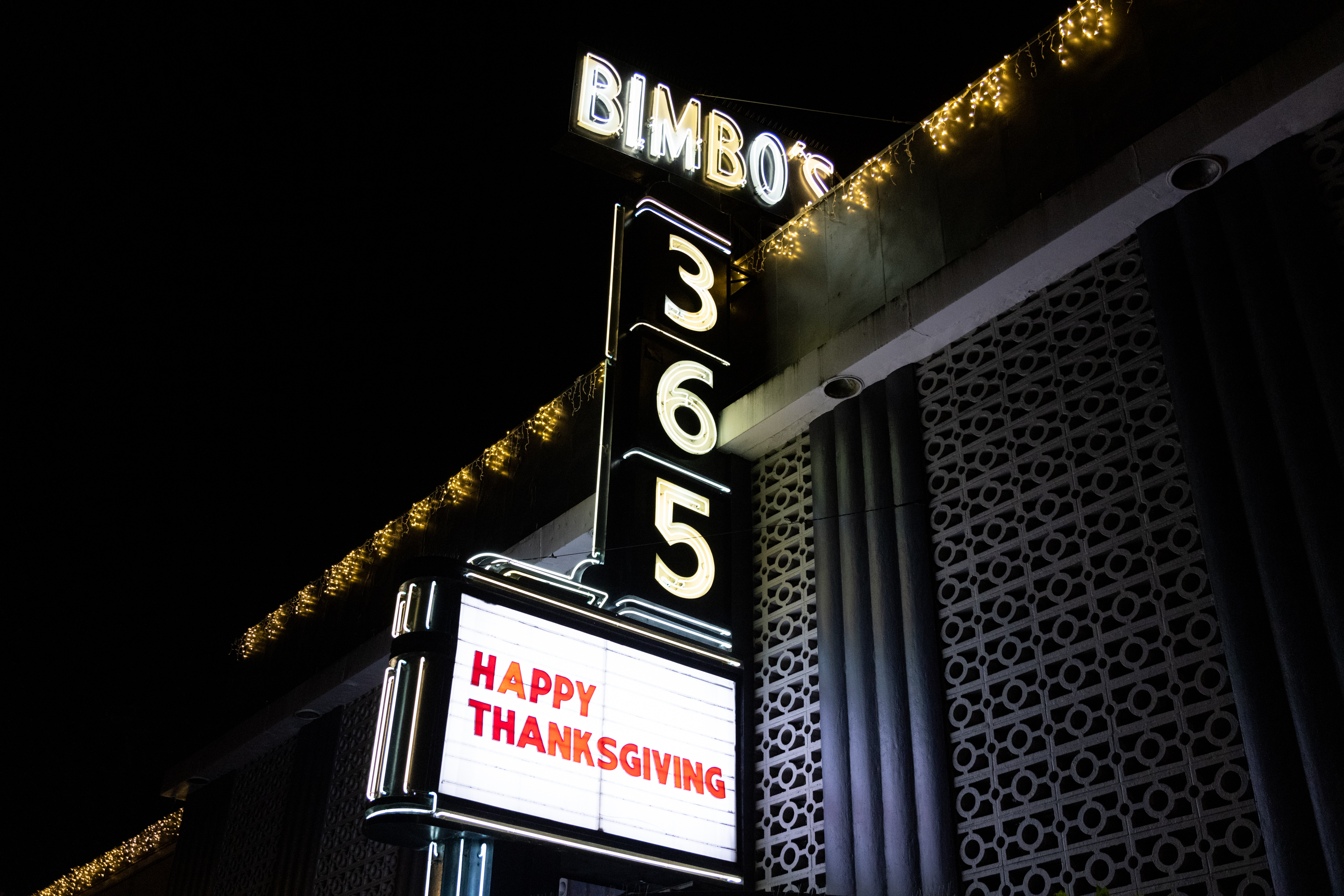 A neon sign at night with the words &quot;Bimbo’s 365&quot; and &quot;HAPPY THANKSGIVING&quot; on the marquee