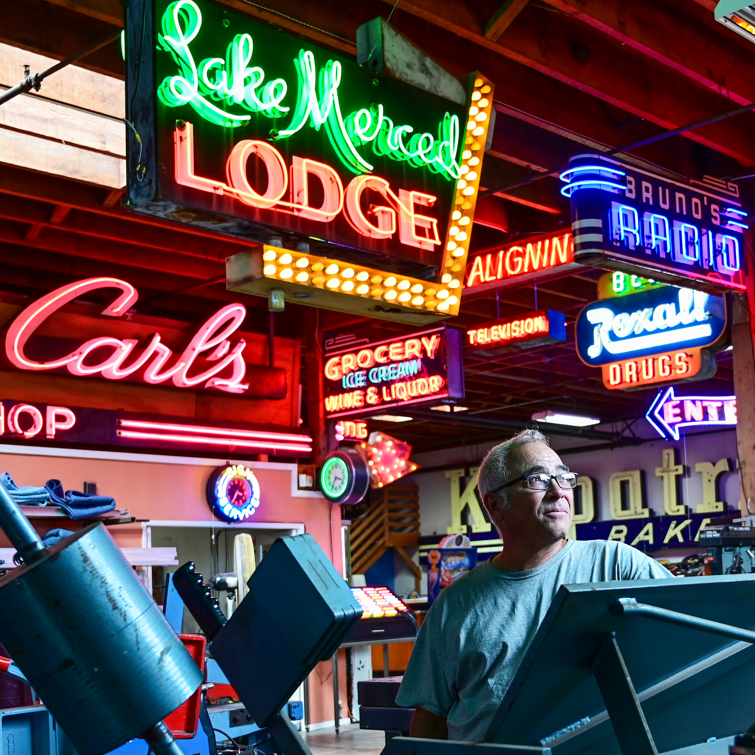 A portrait of a man with a variety of Neon sign in the background of a workshop