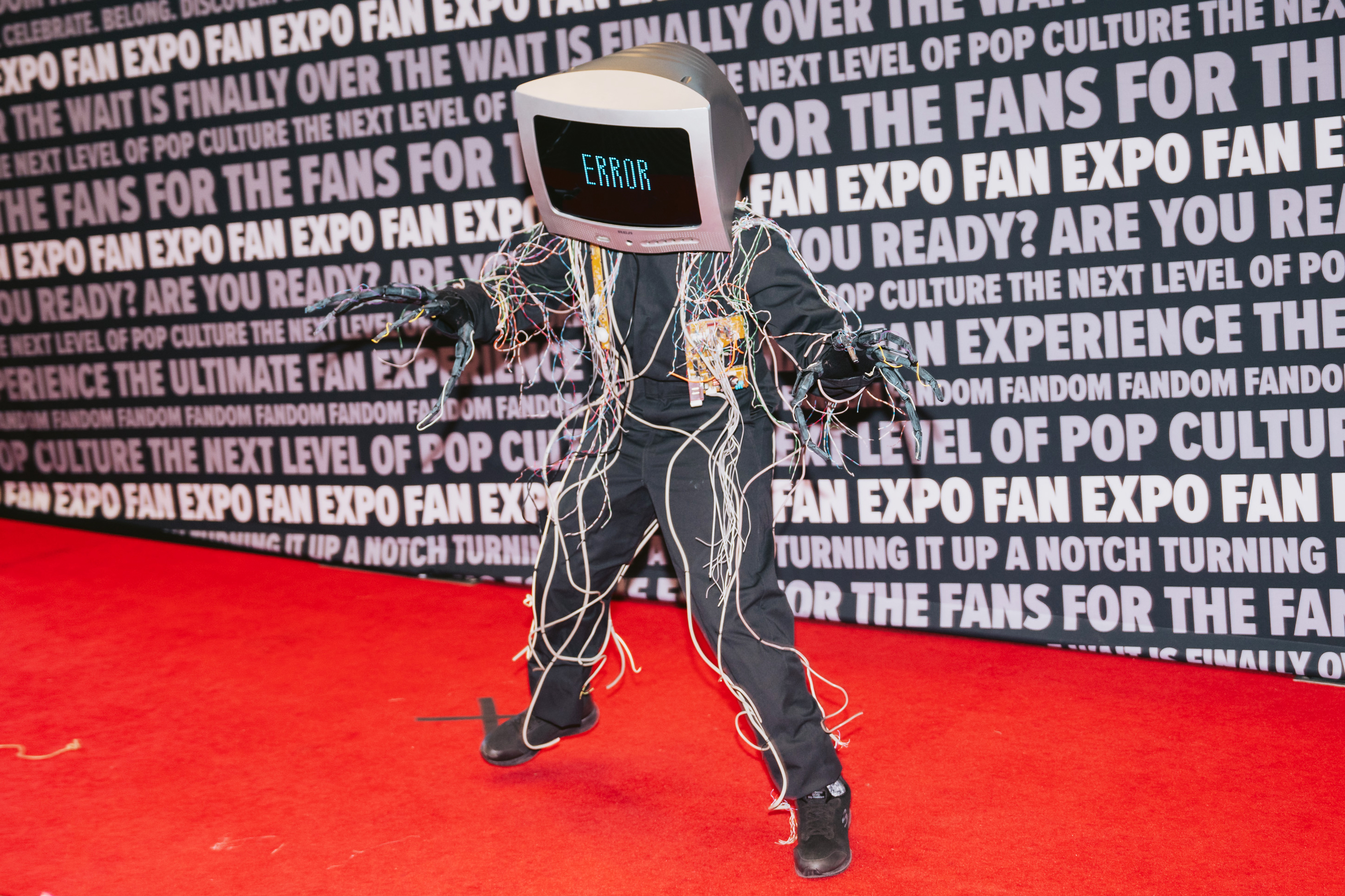 A person wearing a computer on their head while in a costume of cords stands on a red carpet