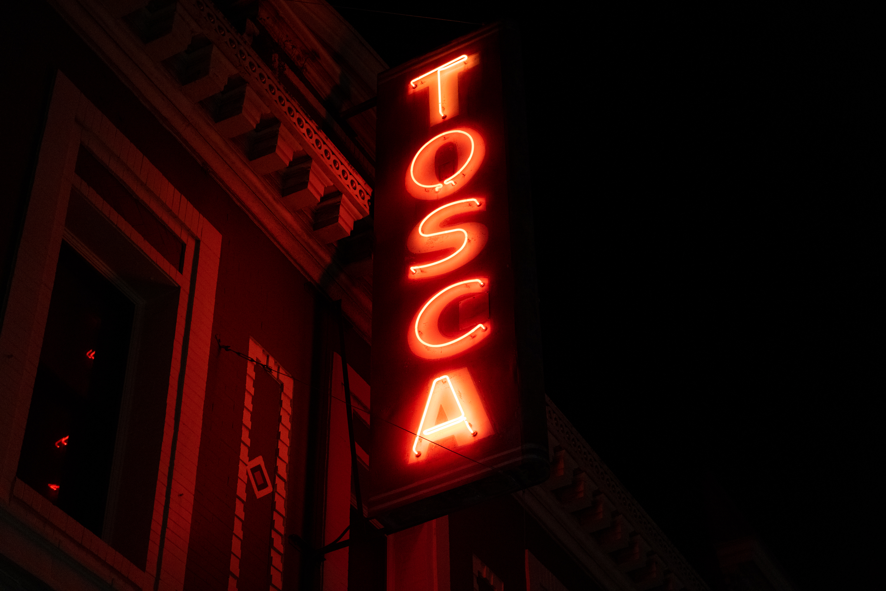 A red neon sign at night that reads &quot;TOSCA&quot;