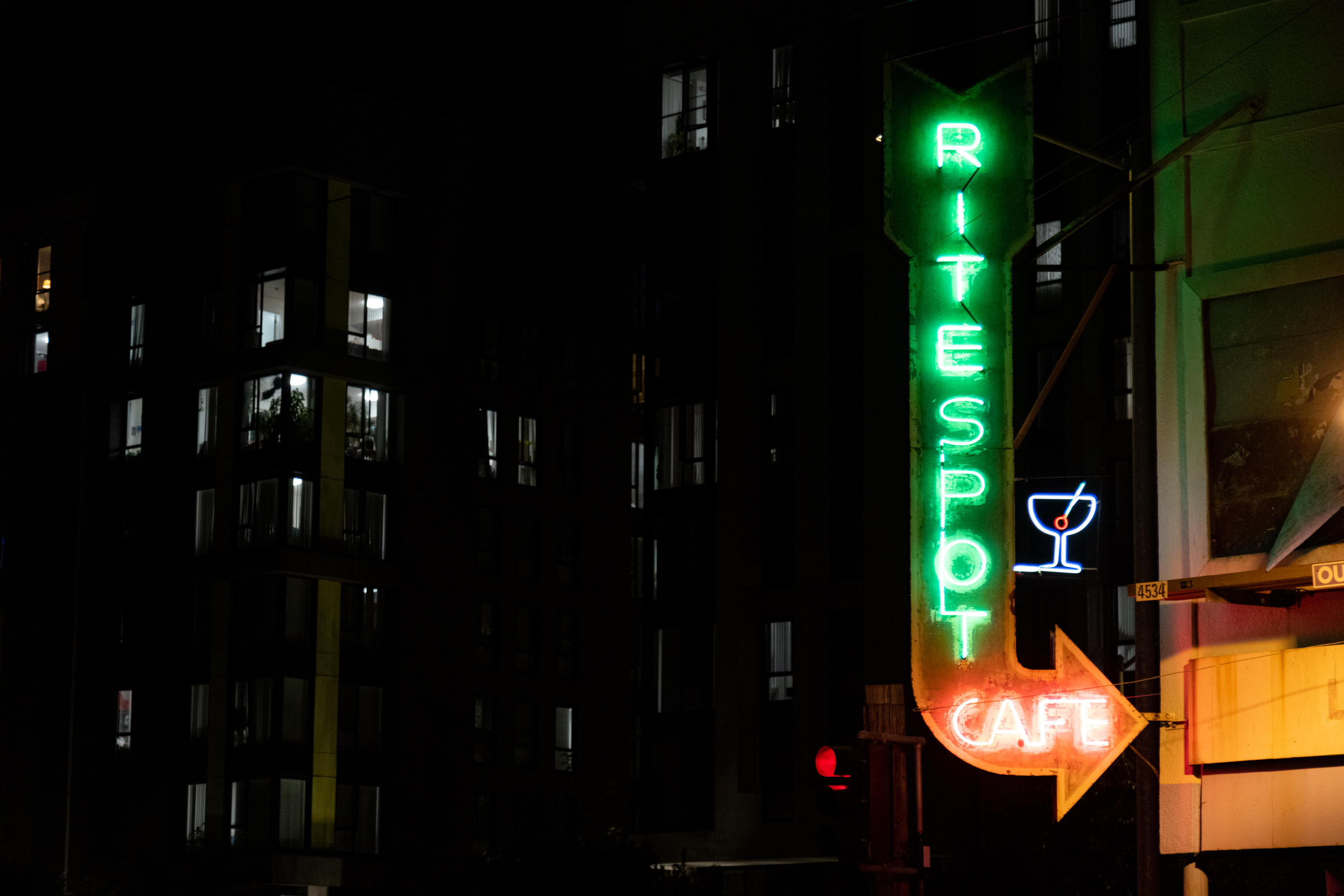 A green neon sign at night that reads &quot;RITESPOT CAFE&quot; in the shape of an arrow pointing downwards and turning right