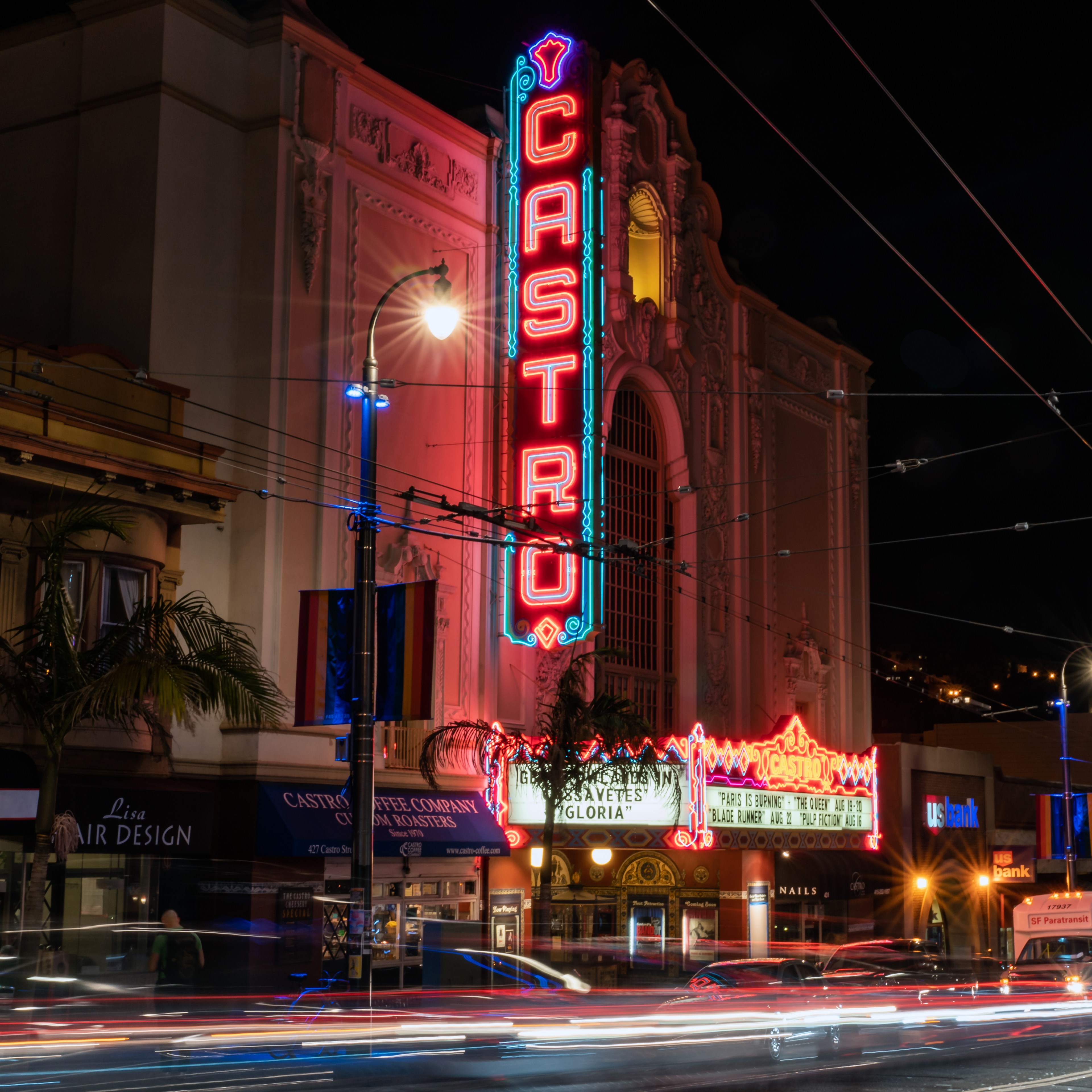The Castro Theatre's neon marquee that reads &quot;CASTRO&quot; lit up during evening hours as cars pass by.