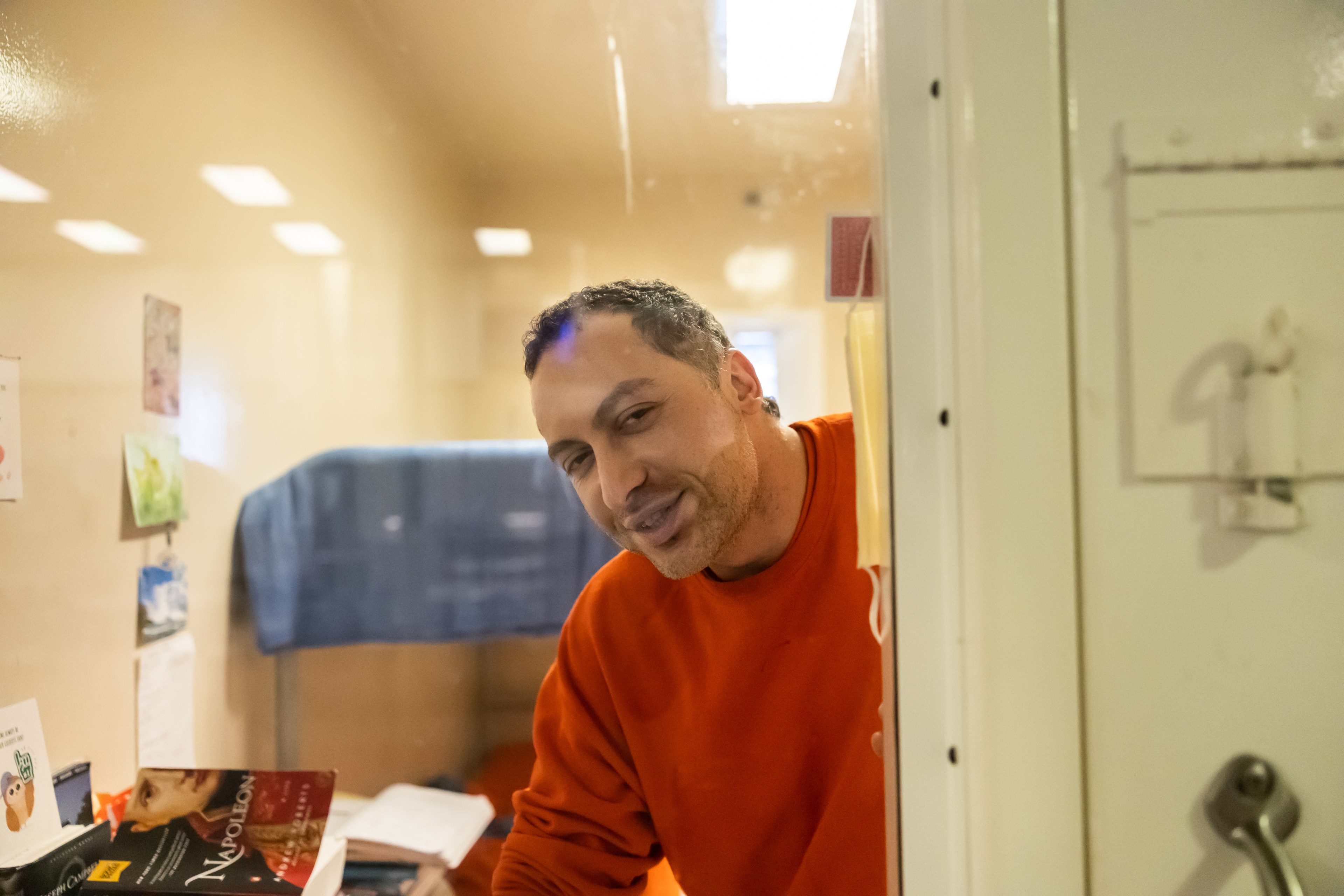 Jail inmate Nima Momeni, suspect for the killing of Cash App founder Bob Lee, while dressed in an orange sweatshirt smiles while looking out the window of his jail cell.