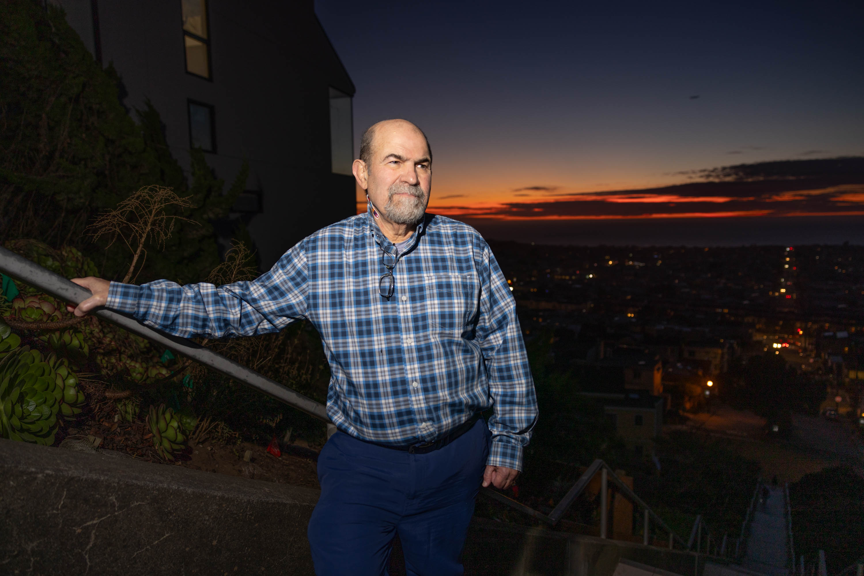A man poses for a portrait on a long staircase during a sunset in the background.