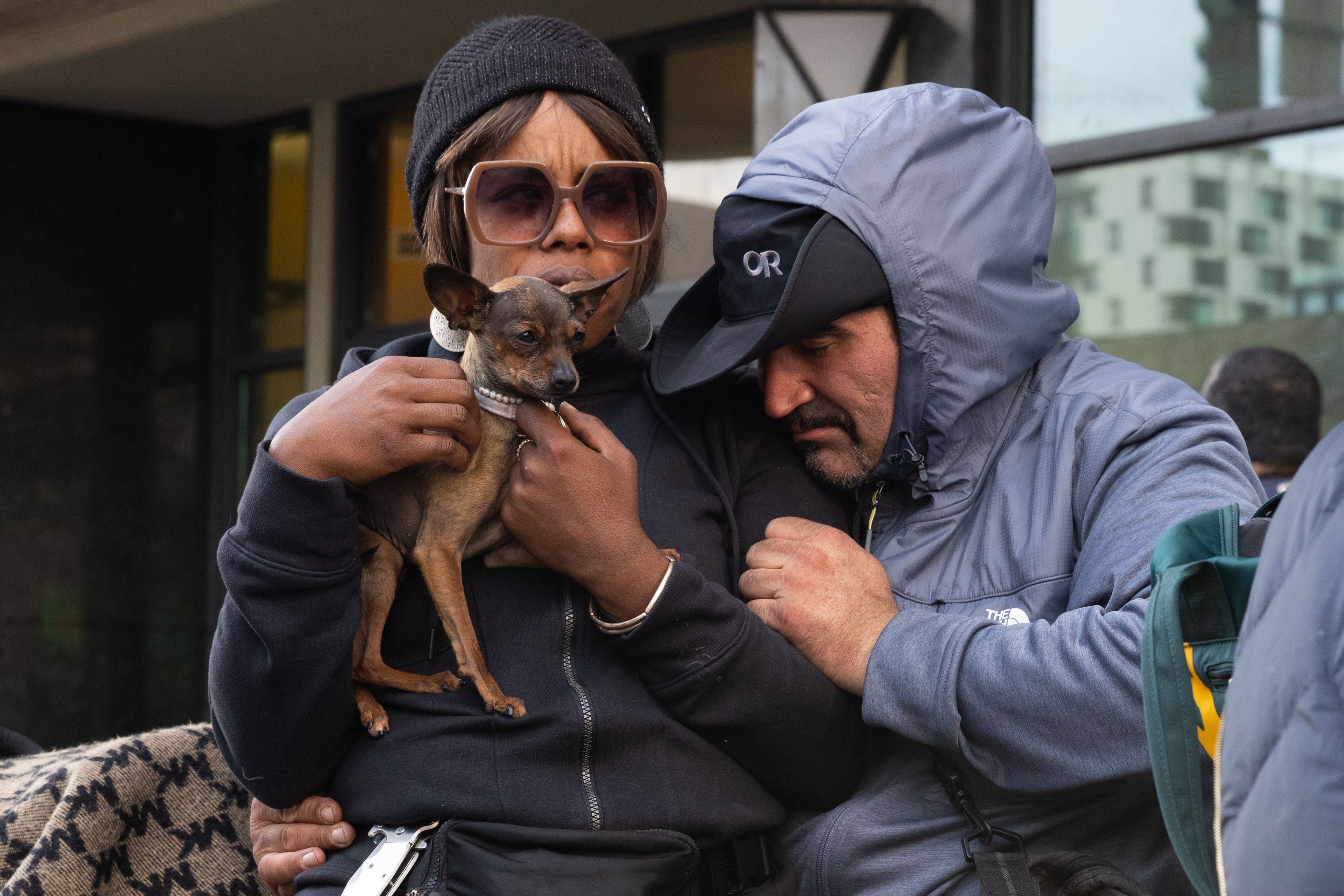 A woman holding a dog sits on a man's lap on sixth street.