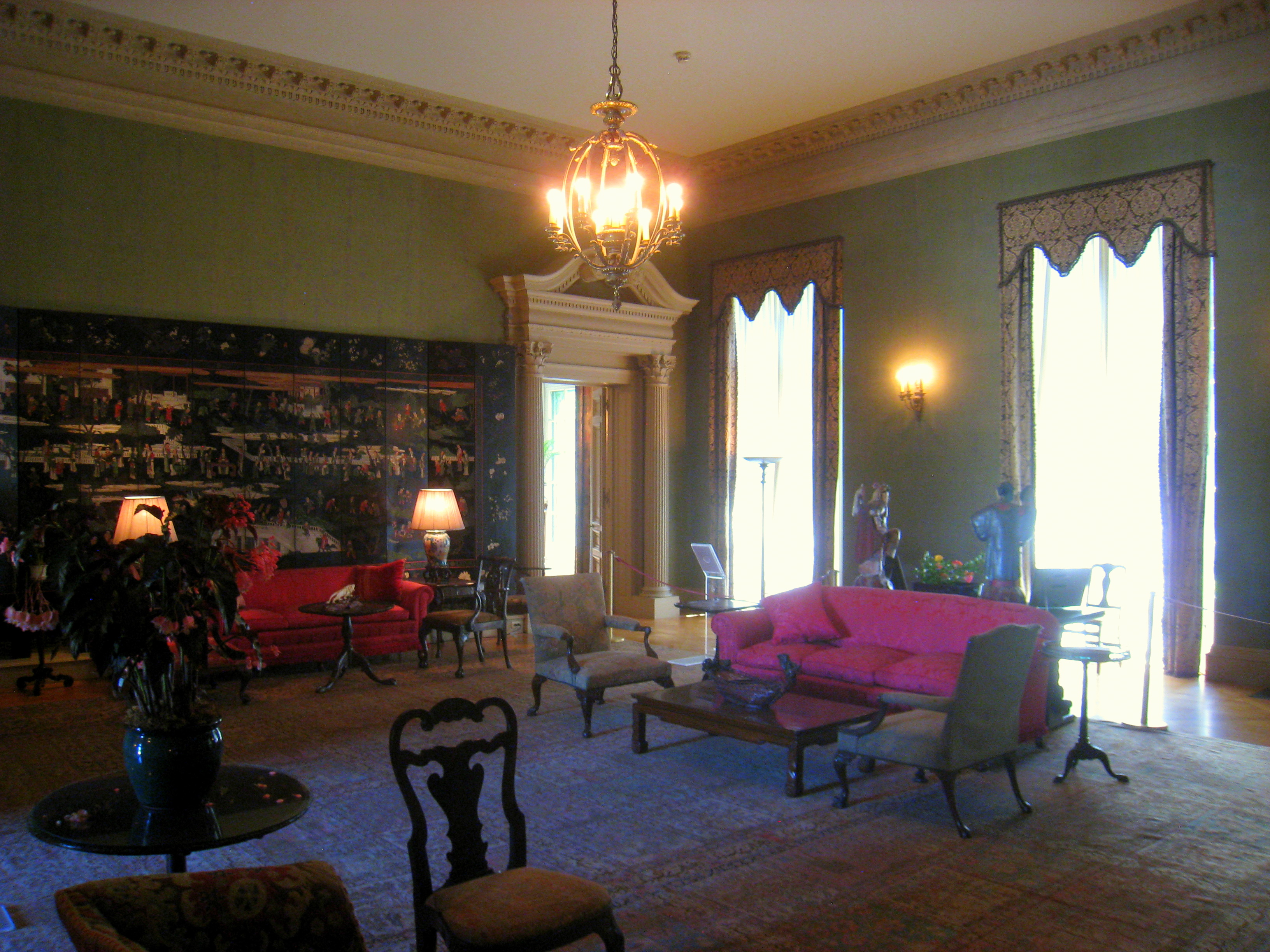 A lowly lit Victorian era room with green wall paper, couches and chairs.
