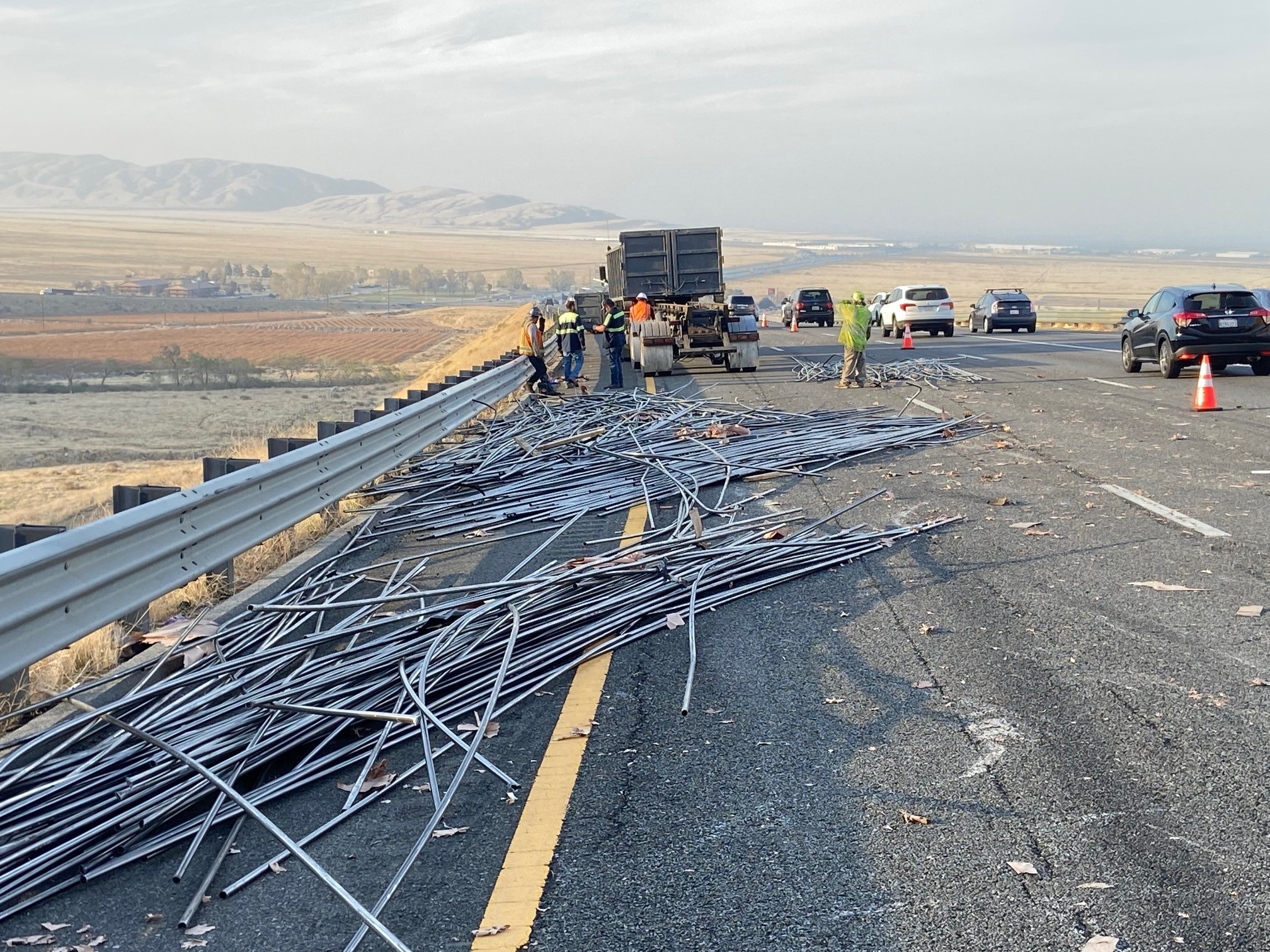 Metal poles spilled on a freeway shoulder with a big-rig parked in the distance.