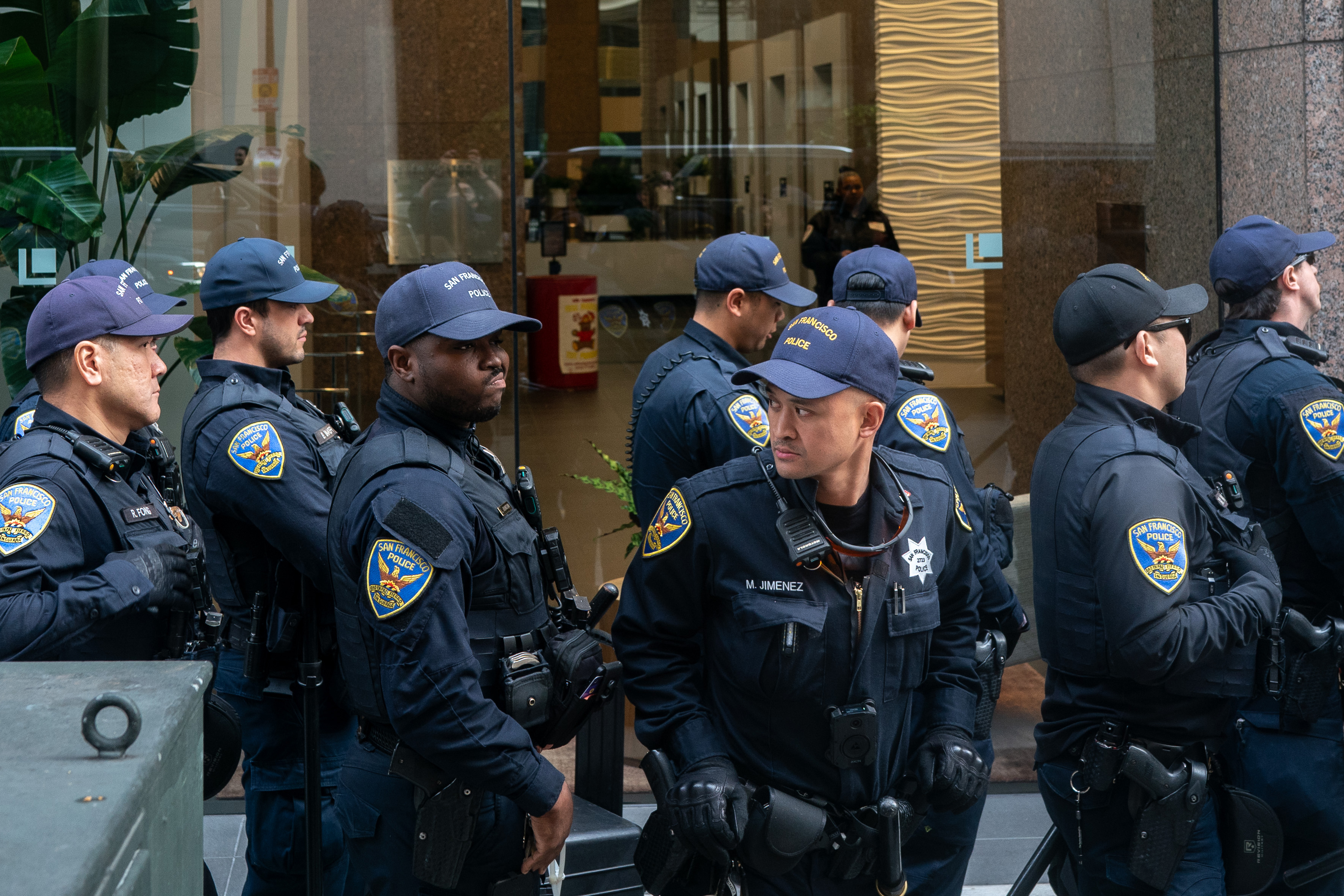 San Francisco Police are seen standing in a line next to a building with a large glass window.