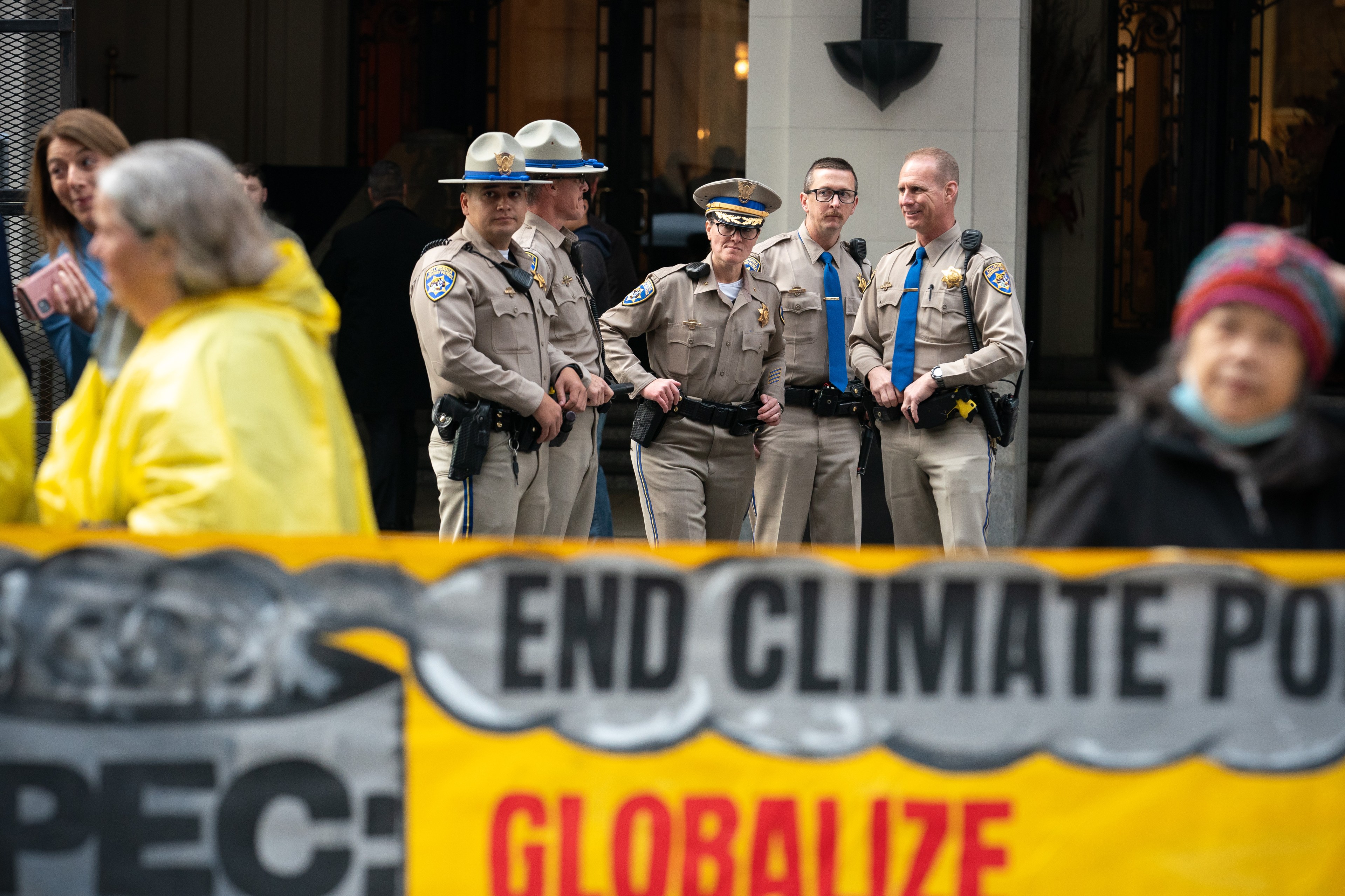 Five California Highway Patrol officers look in the distance of climate activists holding a banner.