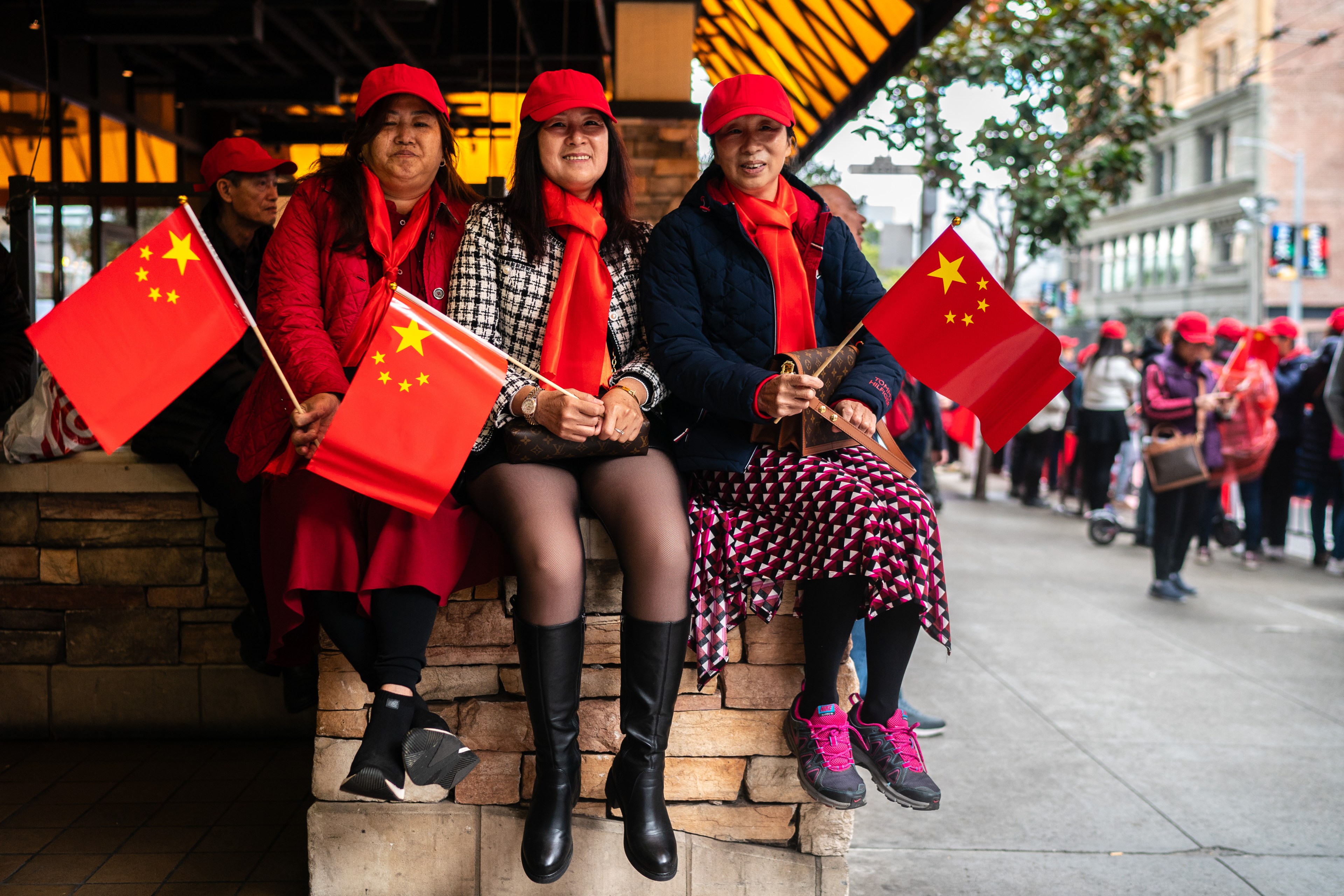 Three woman holding Chinese flags sit on a pedestal on a city street. 