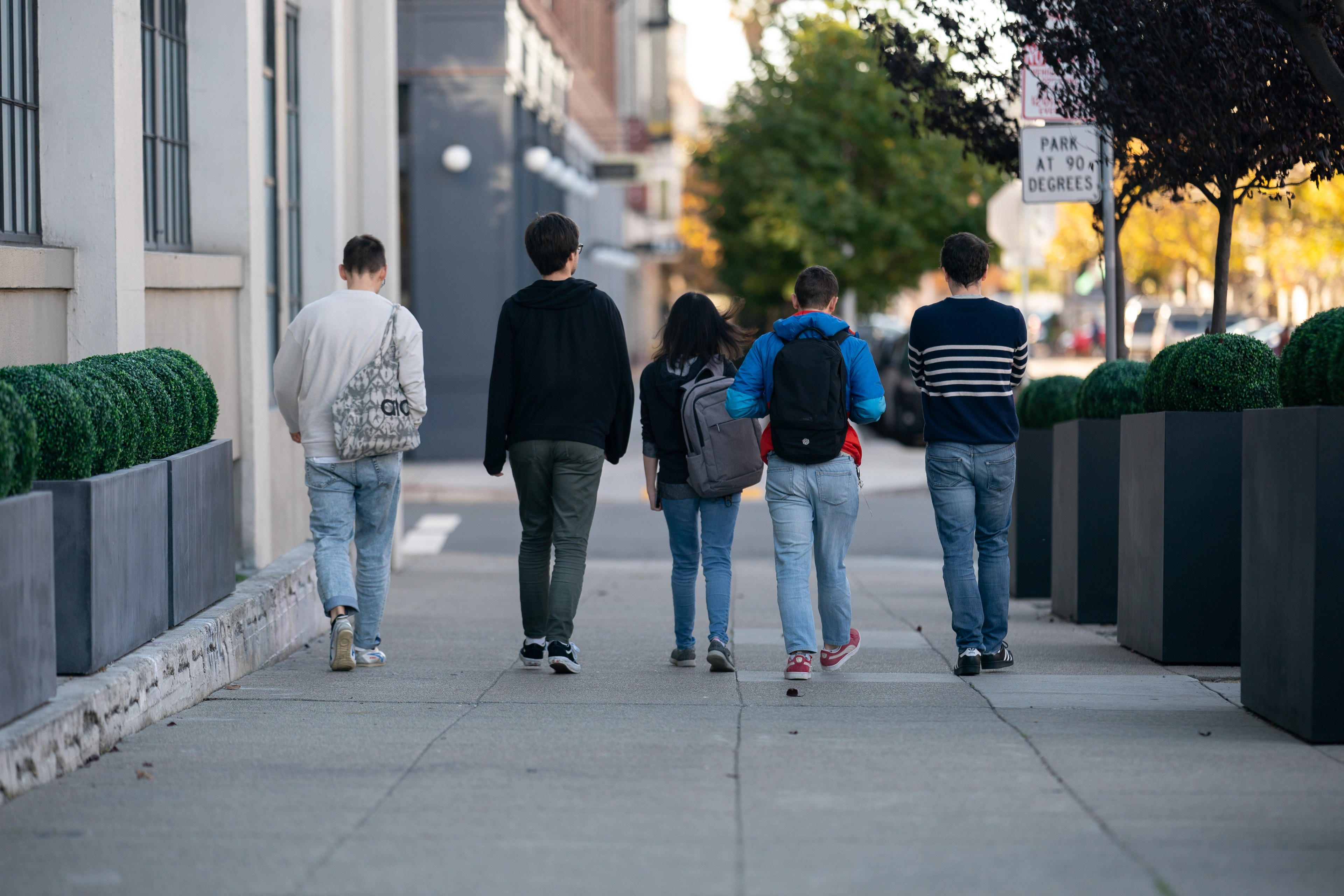 Five young adults walk side by side down a city sidewalk .