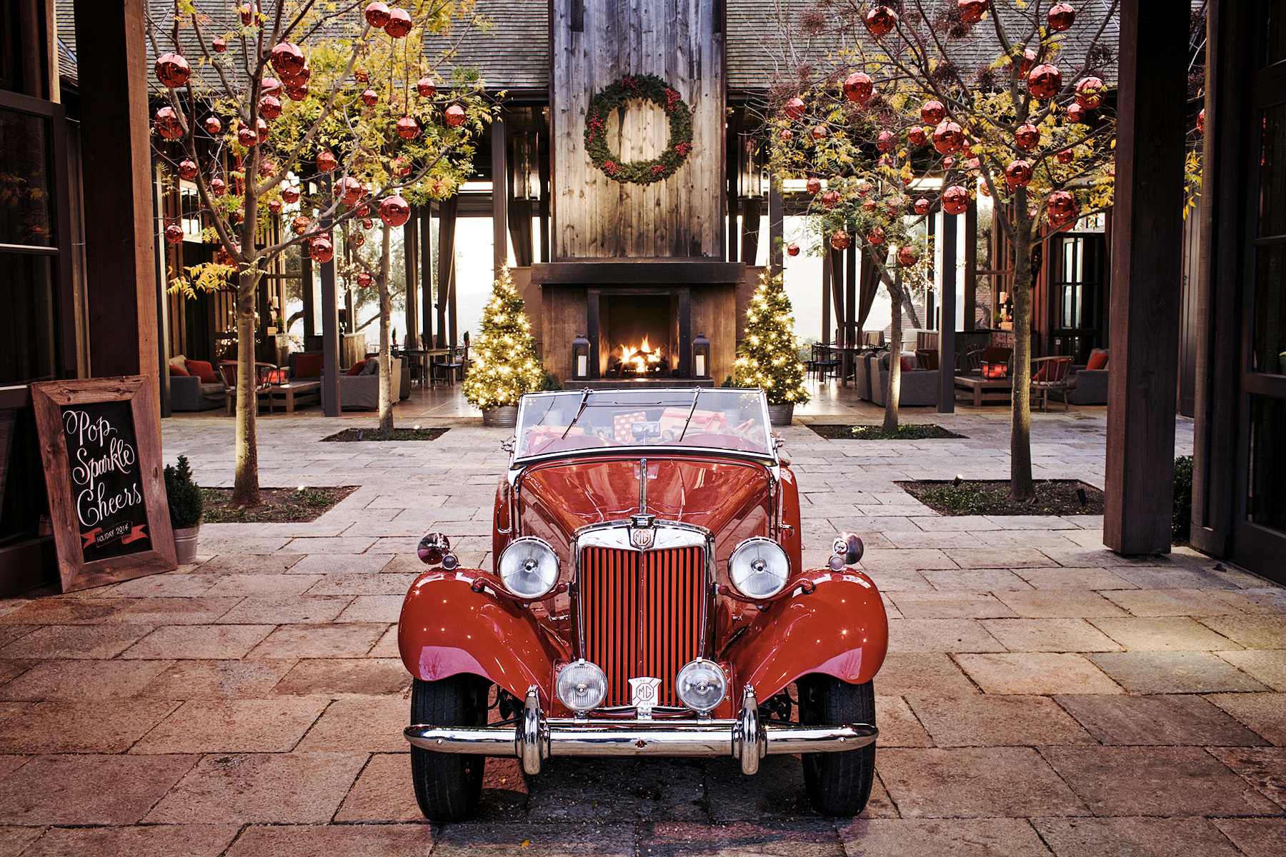 An old-fashioned red car sits under a Christmas wreath.