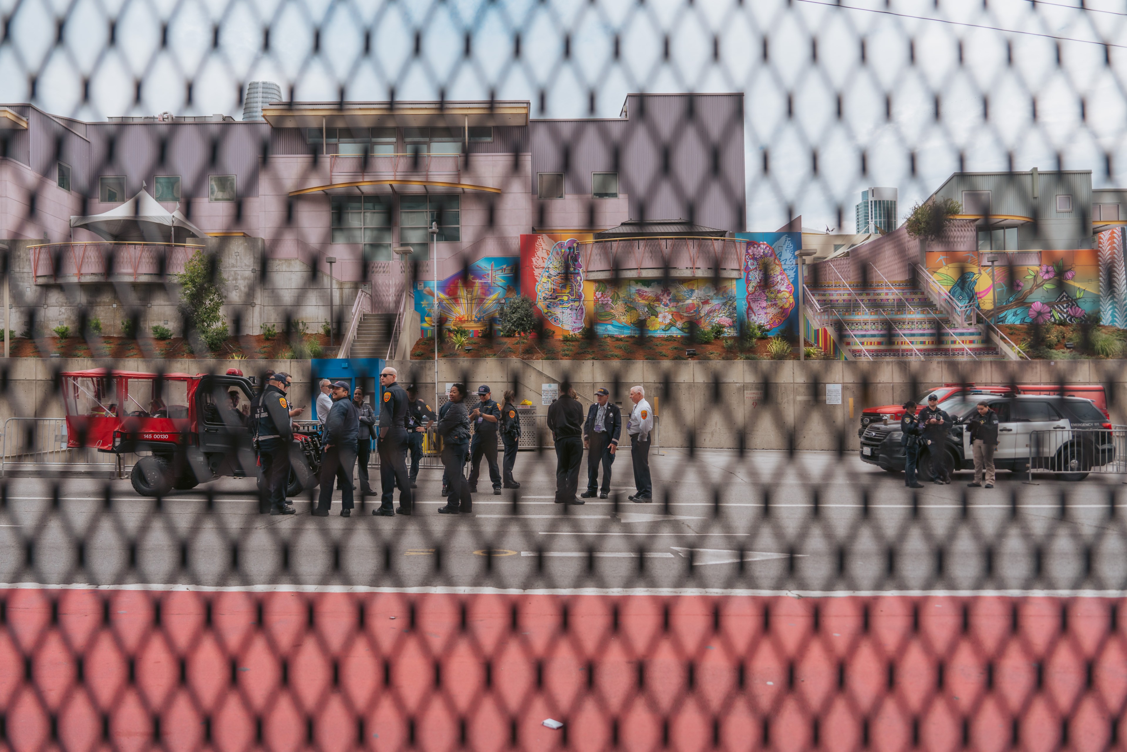 A group of police officers stands on a city street as seem through a metal fence.