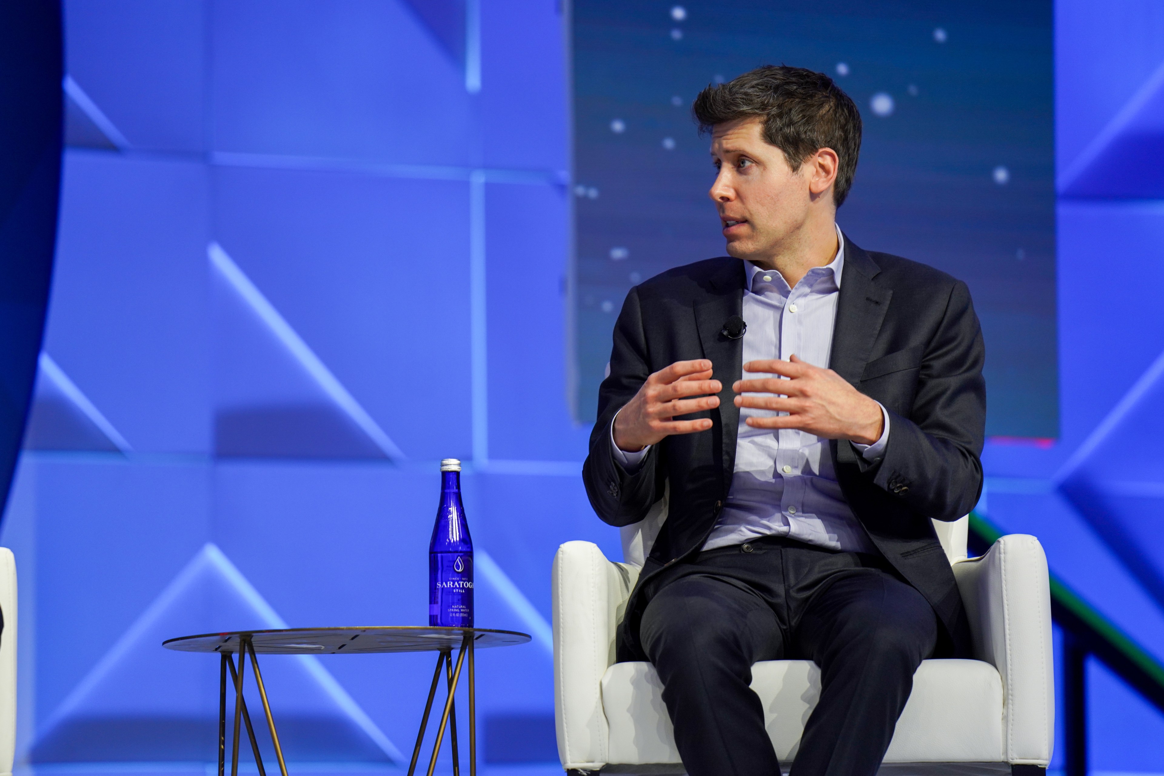 OpenAI CEO Sam Altman, seated in a white chair with a water bottle on a table to his left, speaks at APEC CEO Summit 2023.