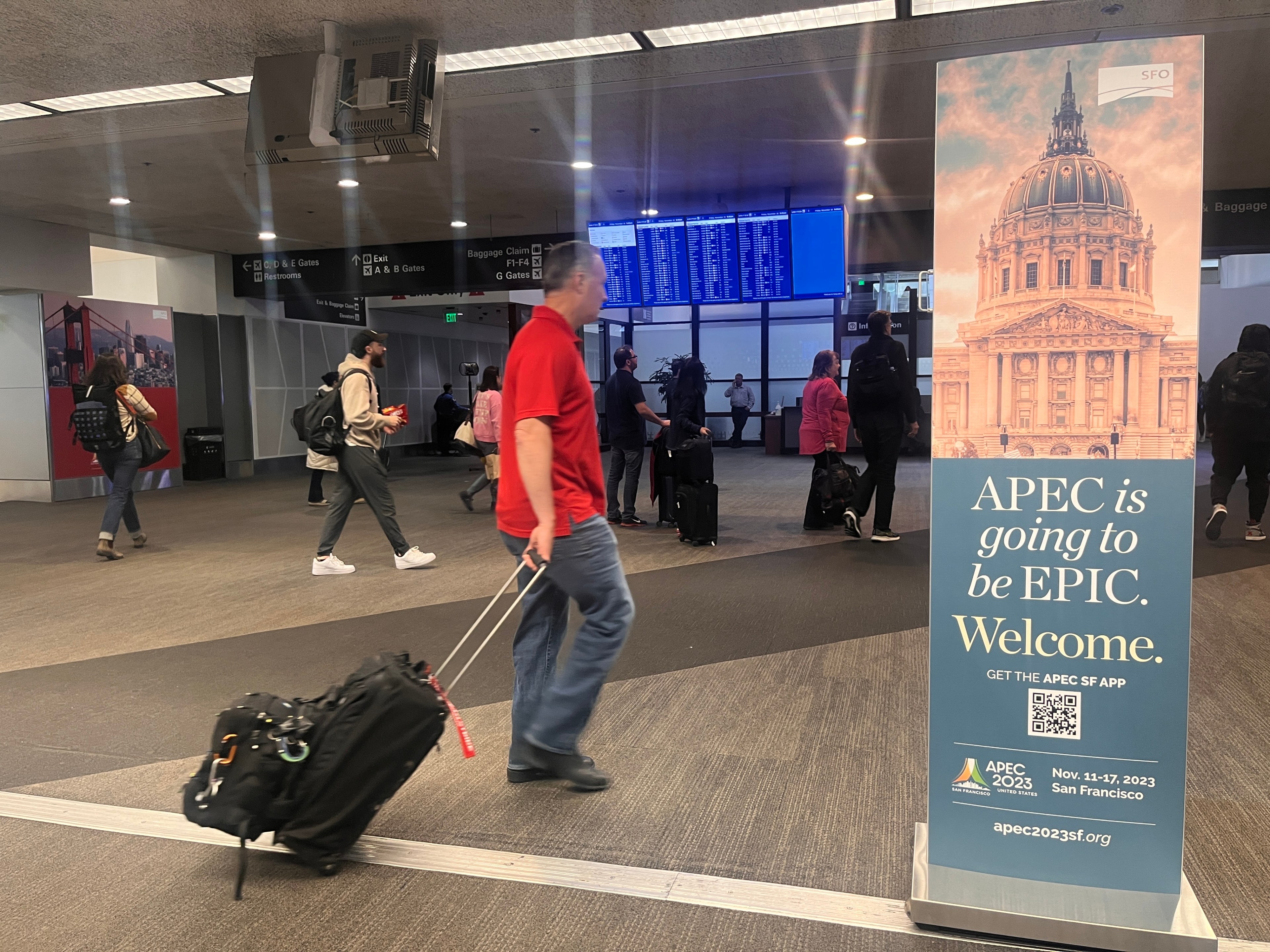 A man with a suitcase passes a sign promoting the APEC summit at San Francisco international airport.