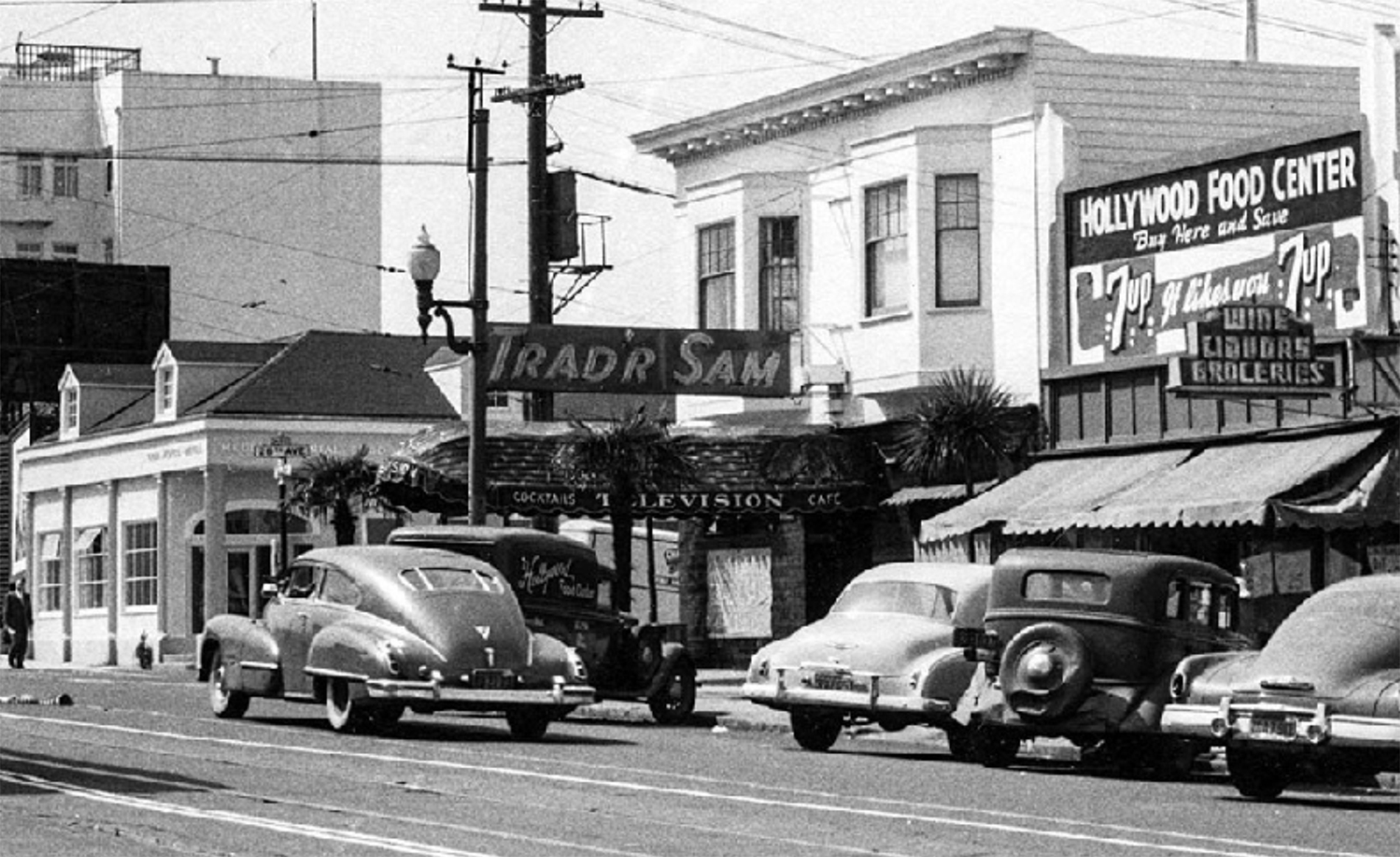 Black and white photo of Geary Boulevard at 26th Avenue in San Francisco with signage that reads Trad'r Sam