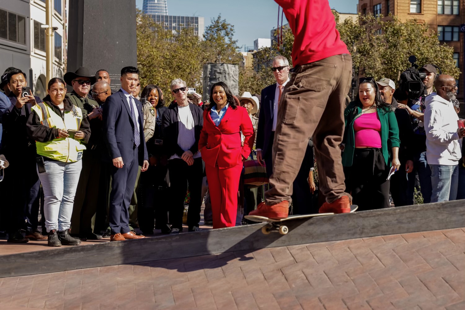 A large group of people including San Francisco Mayor London Breed, watches a skateboarder do a trick on a rail in a newly unveiled skate park in U.N. Plaza on a sunny day in downtown San Francisco.