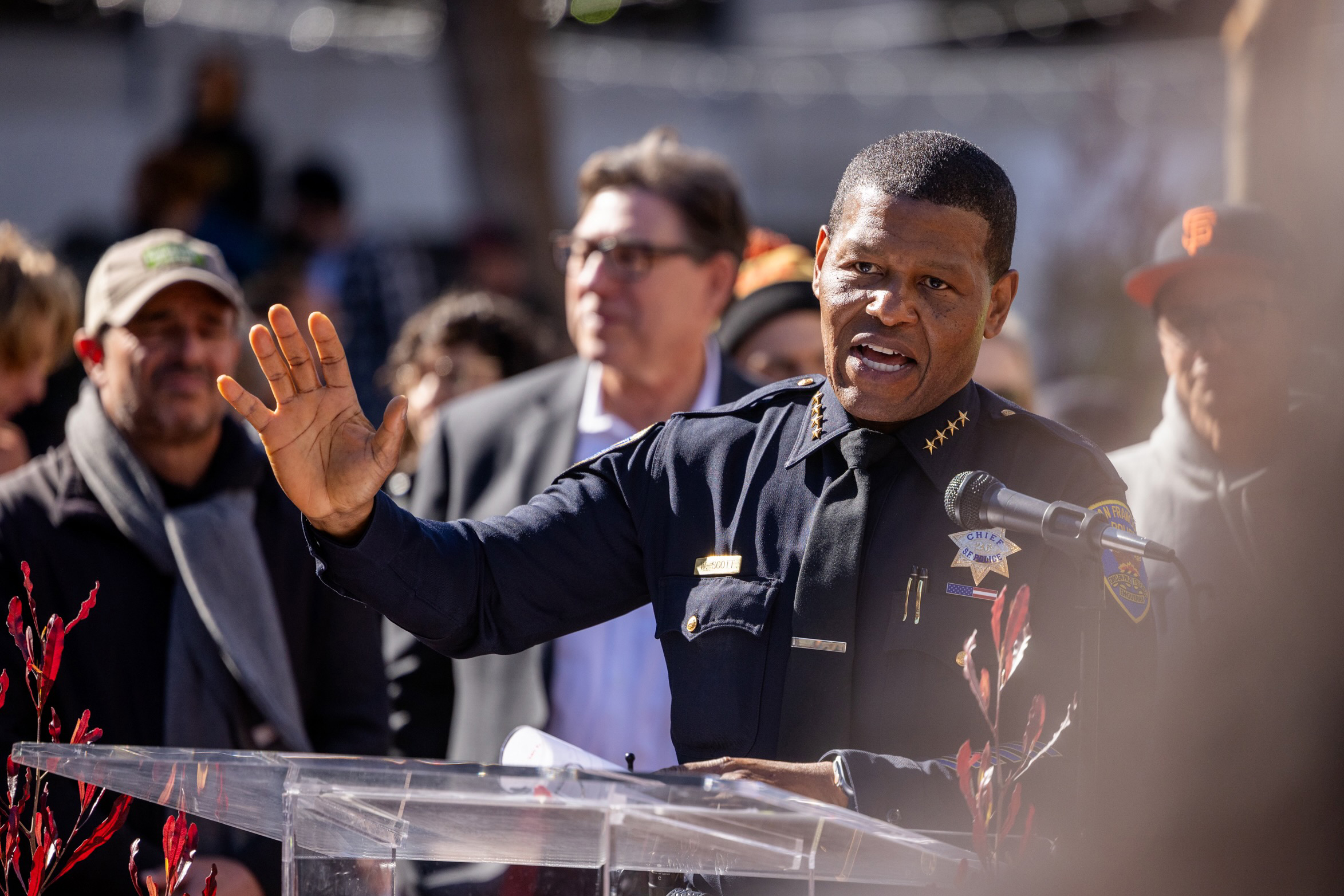 San Francisco Police Department Police Chief Bill Scott, wearing a police uniform holds out his right hand as he gives as speech to a group of people during a press conference to celebrate the reopening of the U.N Plaza which included a skateboard park.