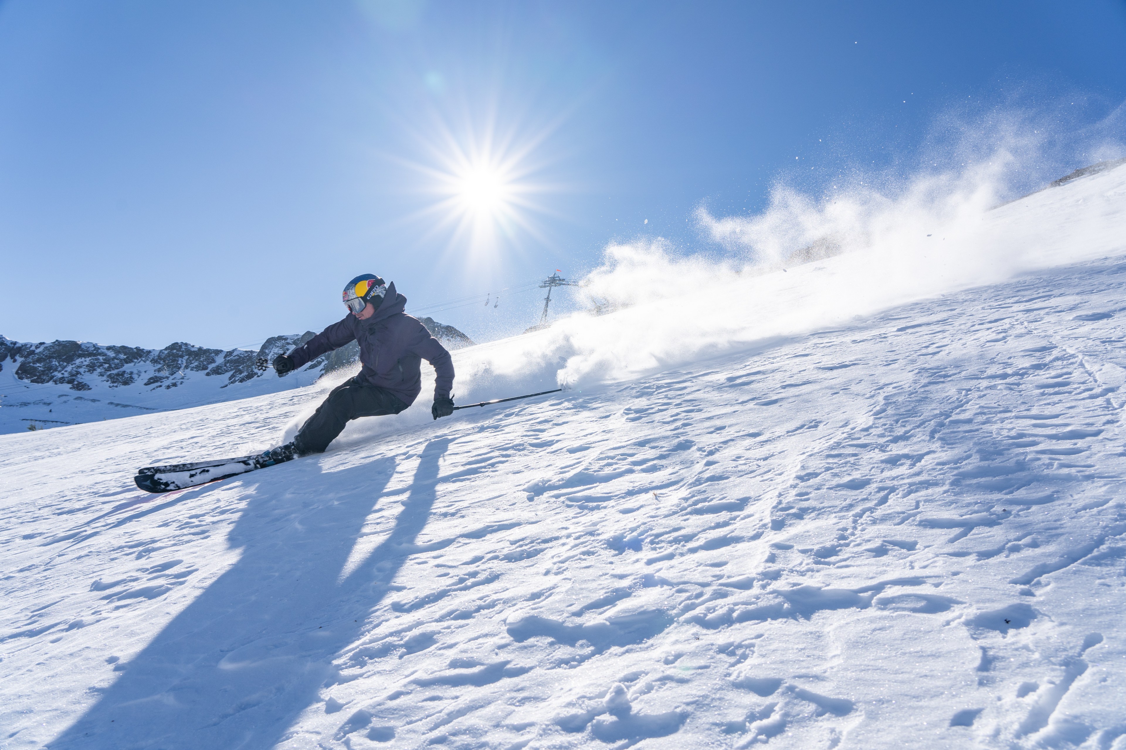 A person skis down the side of a snowy mountain under a sunny sky.