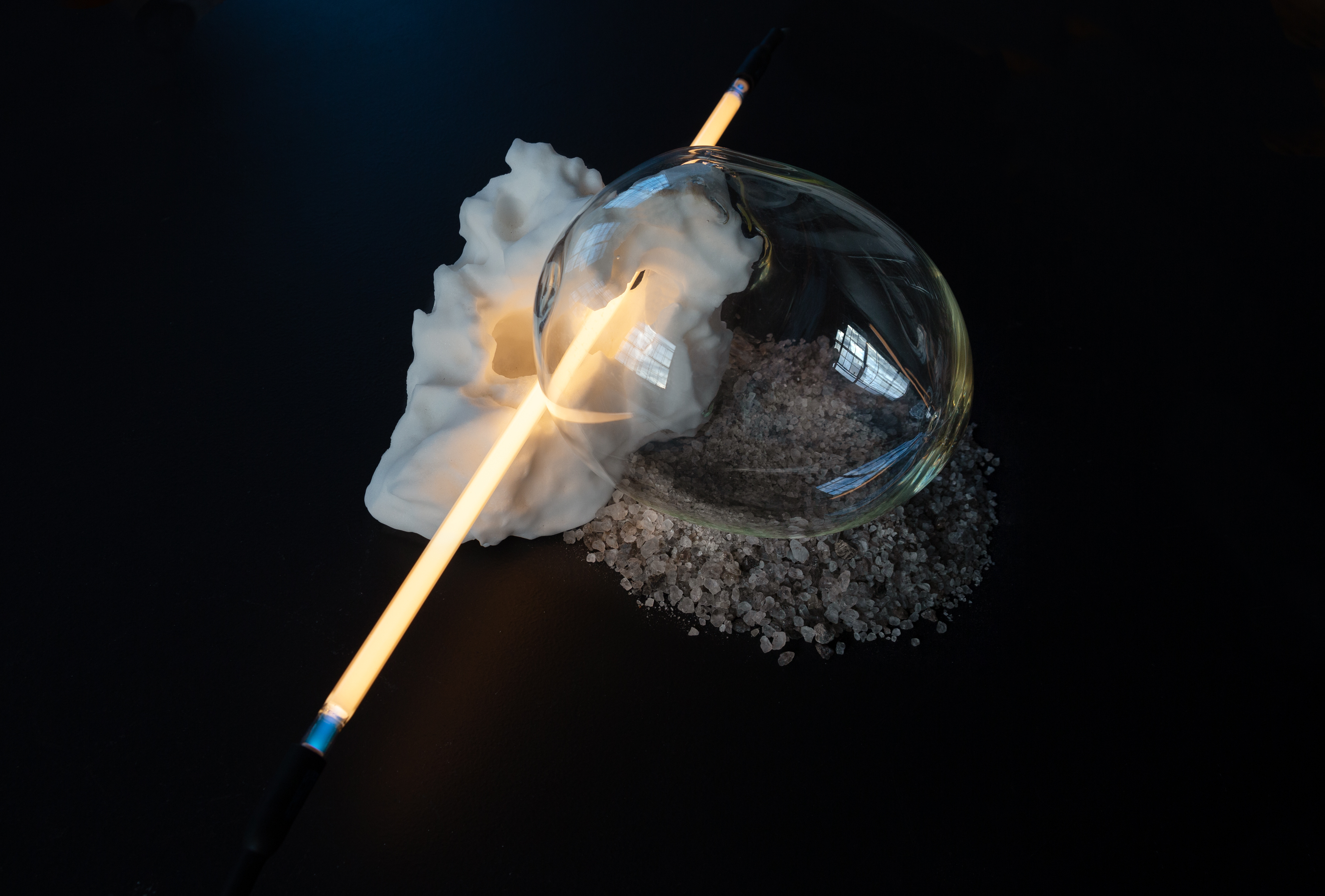 A clear glass bubble is attached to a white glowing neon tube and a block of carved salt.