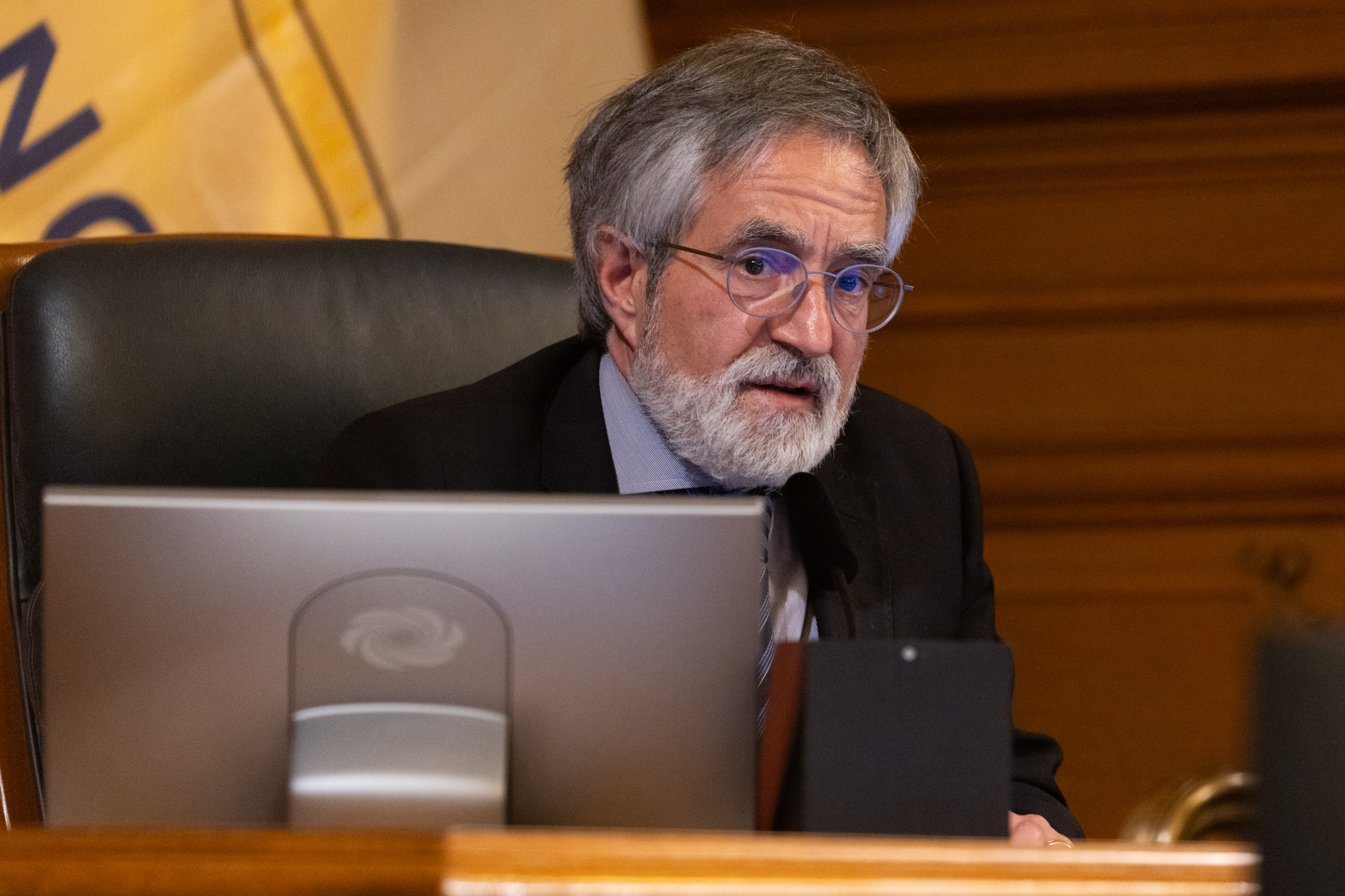 Supervisor Aaron Peskin looks forward in a suit at his chair during the Board of Supervisors public comment at city hall.