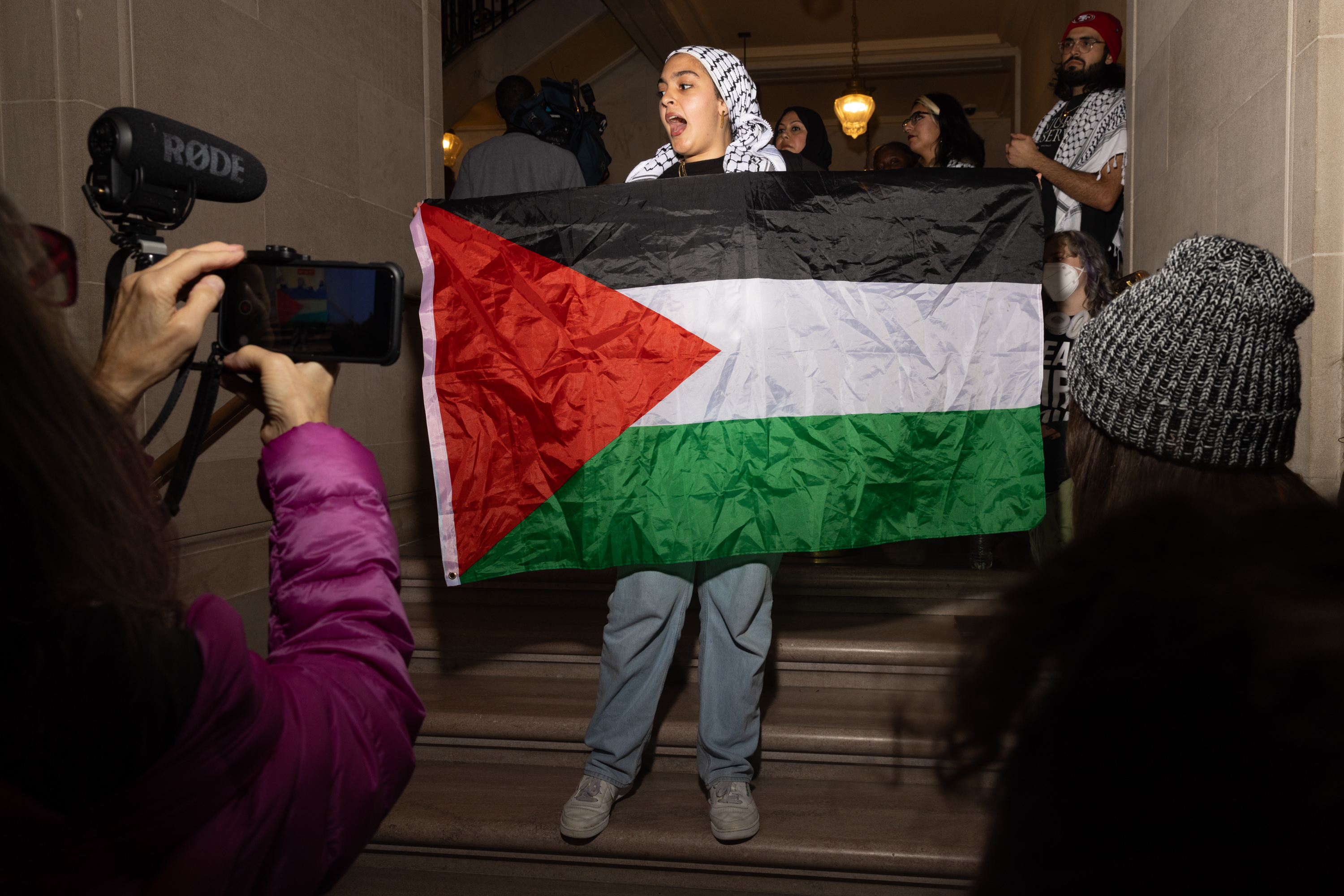 A person holds a Palestinian flag on inside city hall.