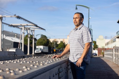 A man a gray bottom shirt poses for a portrait along a bridge