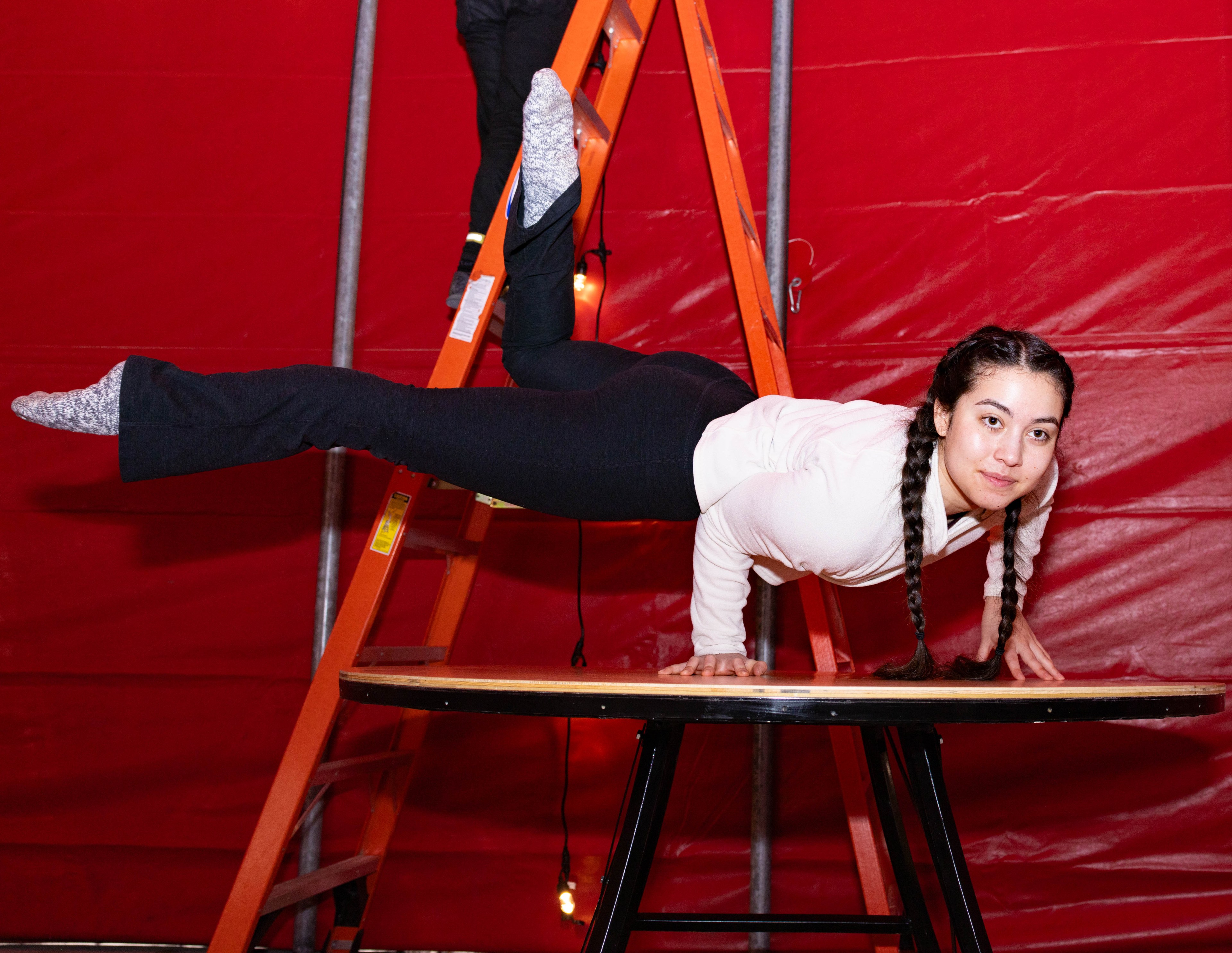 A person on their hands and legs in the air on top of a table inside a red tent.