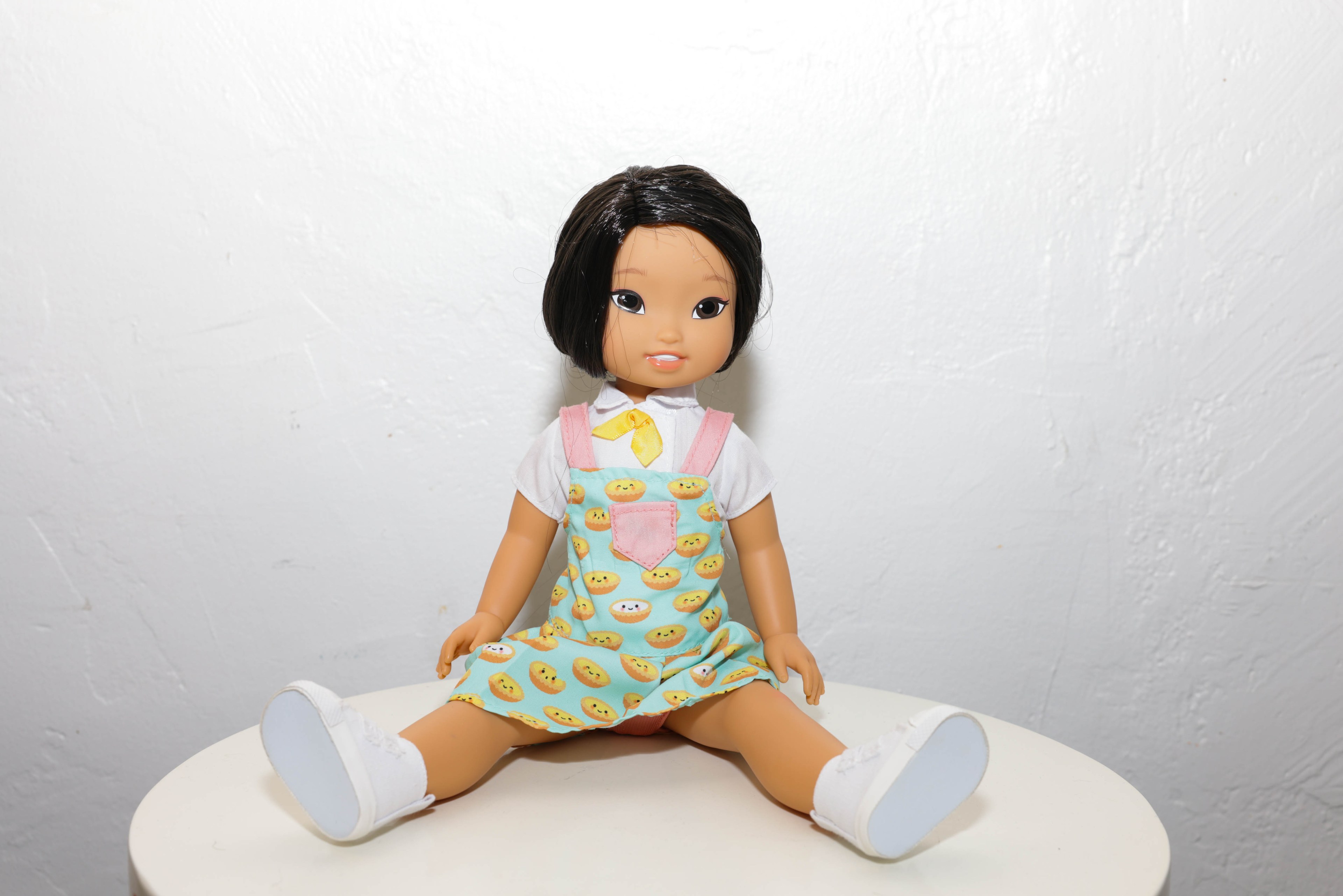 A doll sits on top of a white table in a green dress and white shoes. 