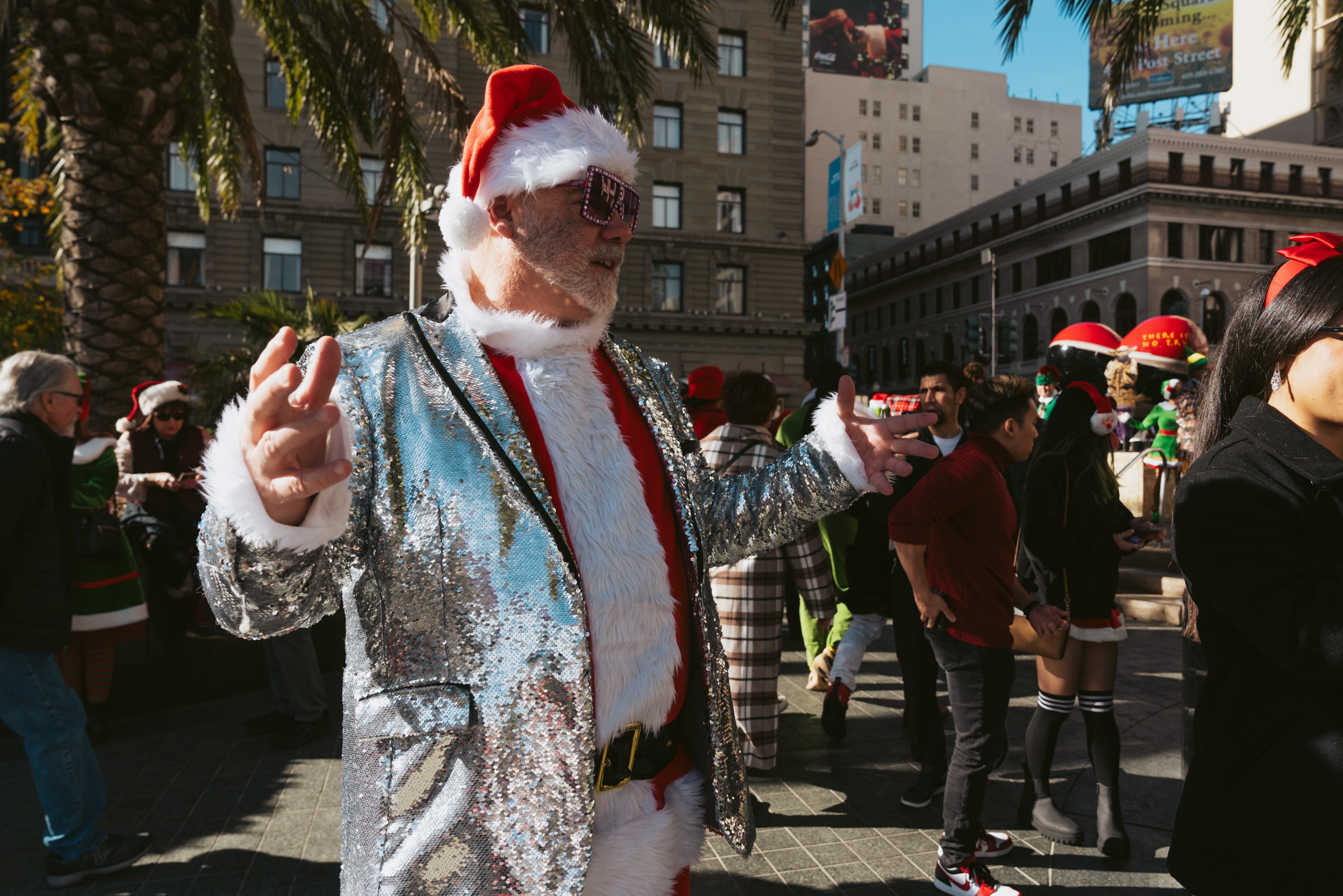A man in a Santa hat and silver-sequined blazer gesticulates while he talks.