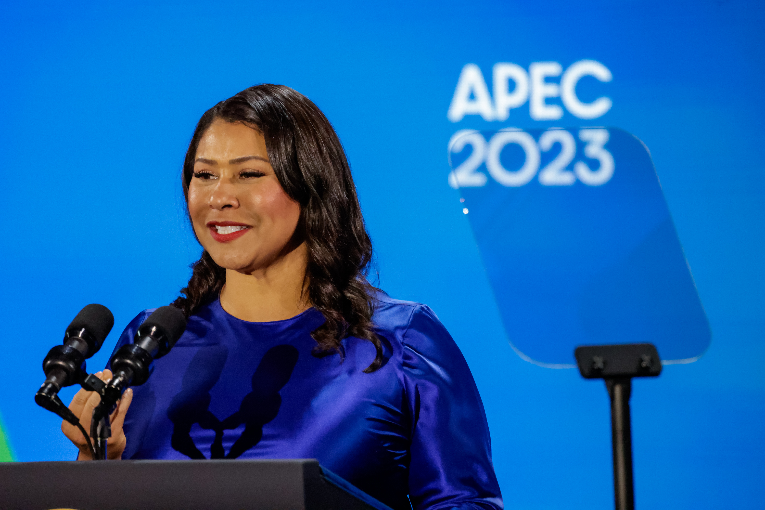 A woman is speaking at a podium with "APEC 2023" in the background.