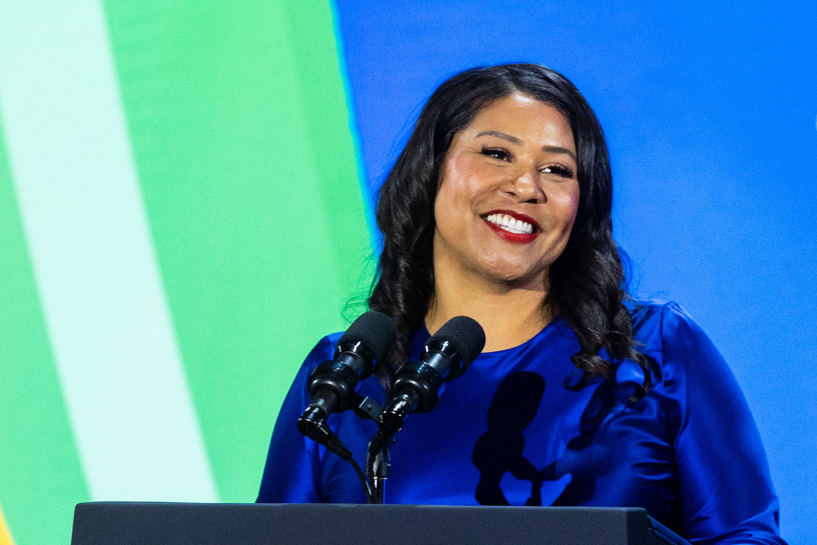 Woman smiles while speaking into microphone in front of green and blue background