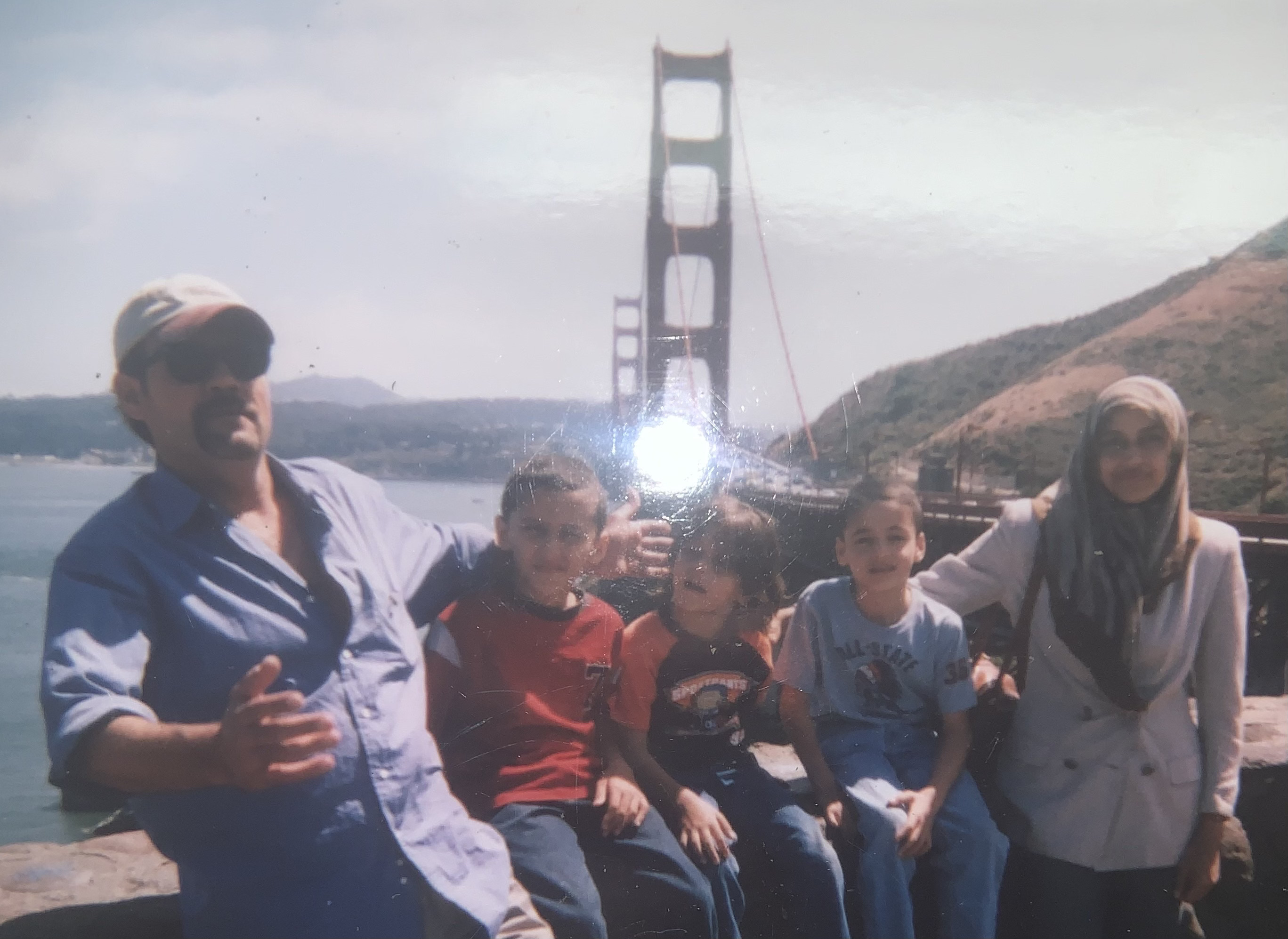 man in white hat and blue shirt and woman in hijab and white shirt with three children in front of the golden gate bridge