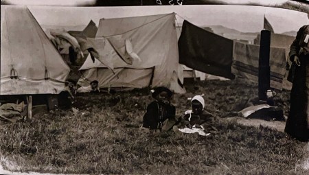 Two children sit in grass in front of makeshift tents up in San Francisco after the 1906 earthquake.
