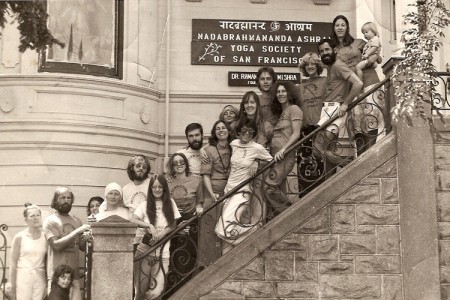 A black and white photograph of a group of people standing on stops with a sign that reads &quot;Yoga Society of San Francisco&quot; behind them.