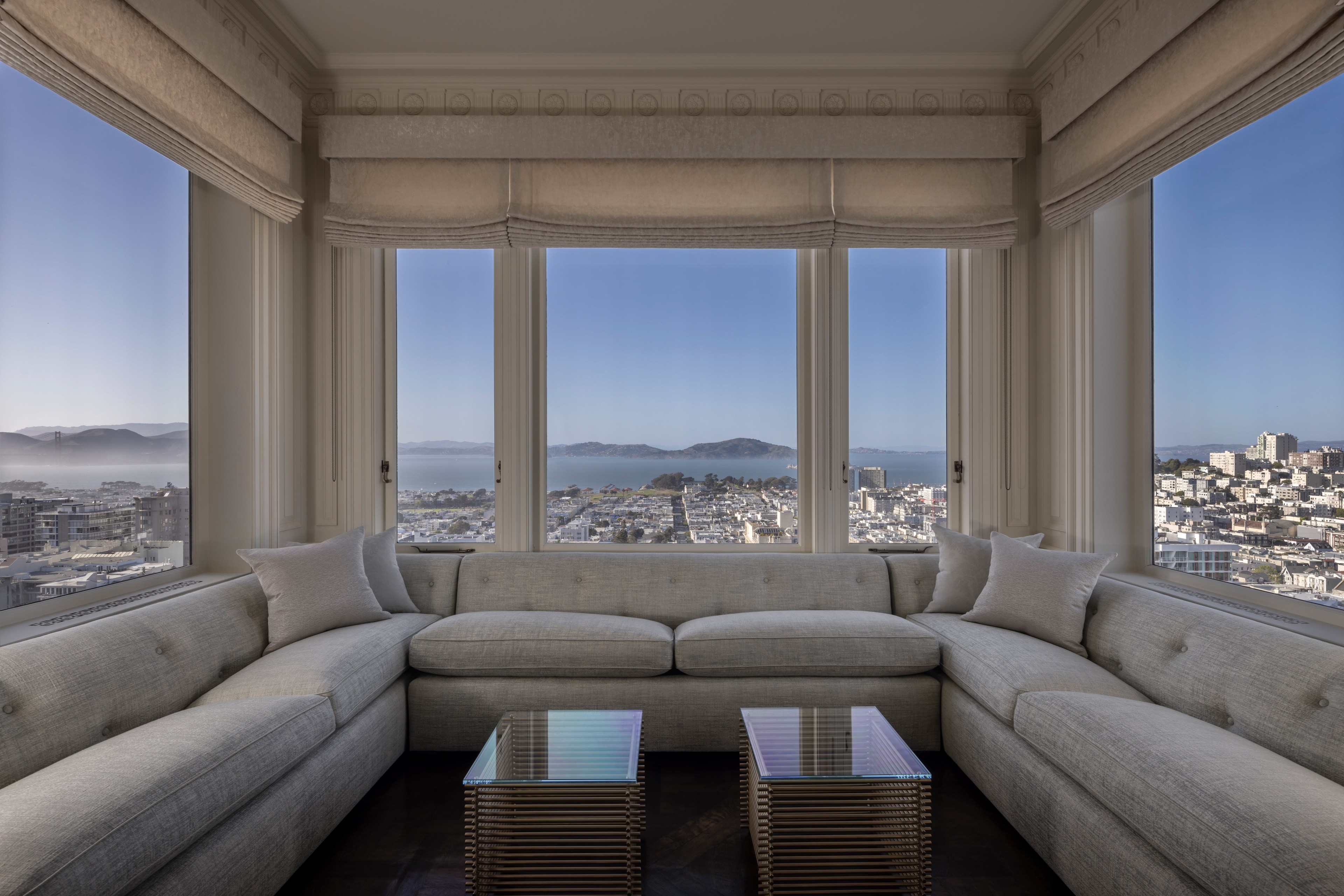 San Francisco's northern skyline is visible from several windows in a nook lined with soft gray couch seating and two small tables.