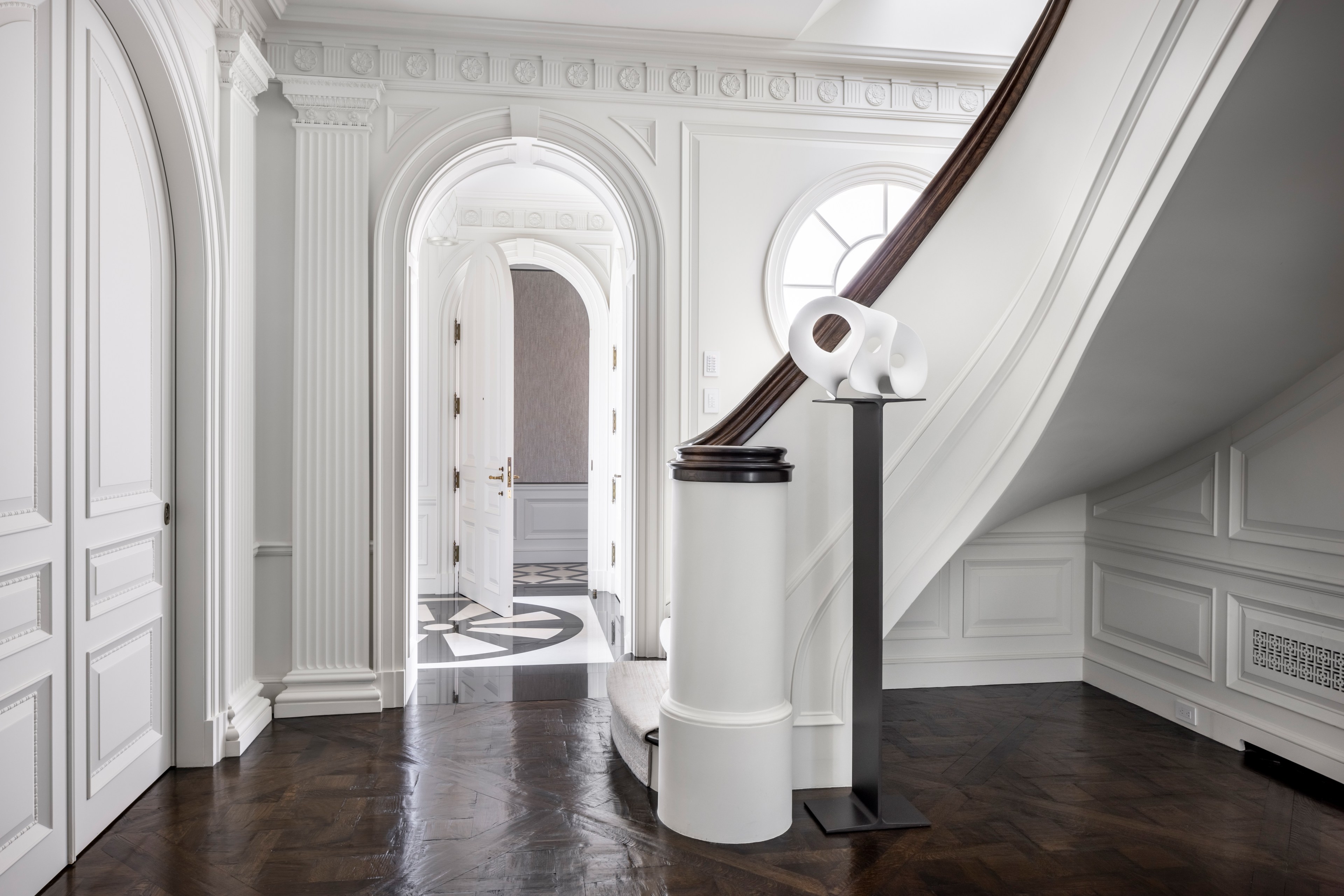 Arched doorways and paneled walls with columns carved into surfaces stand out in a hallway with a staircase.