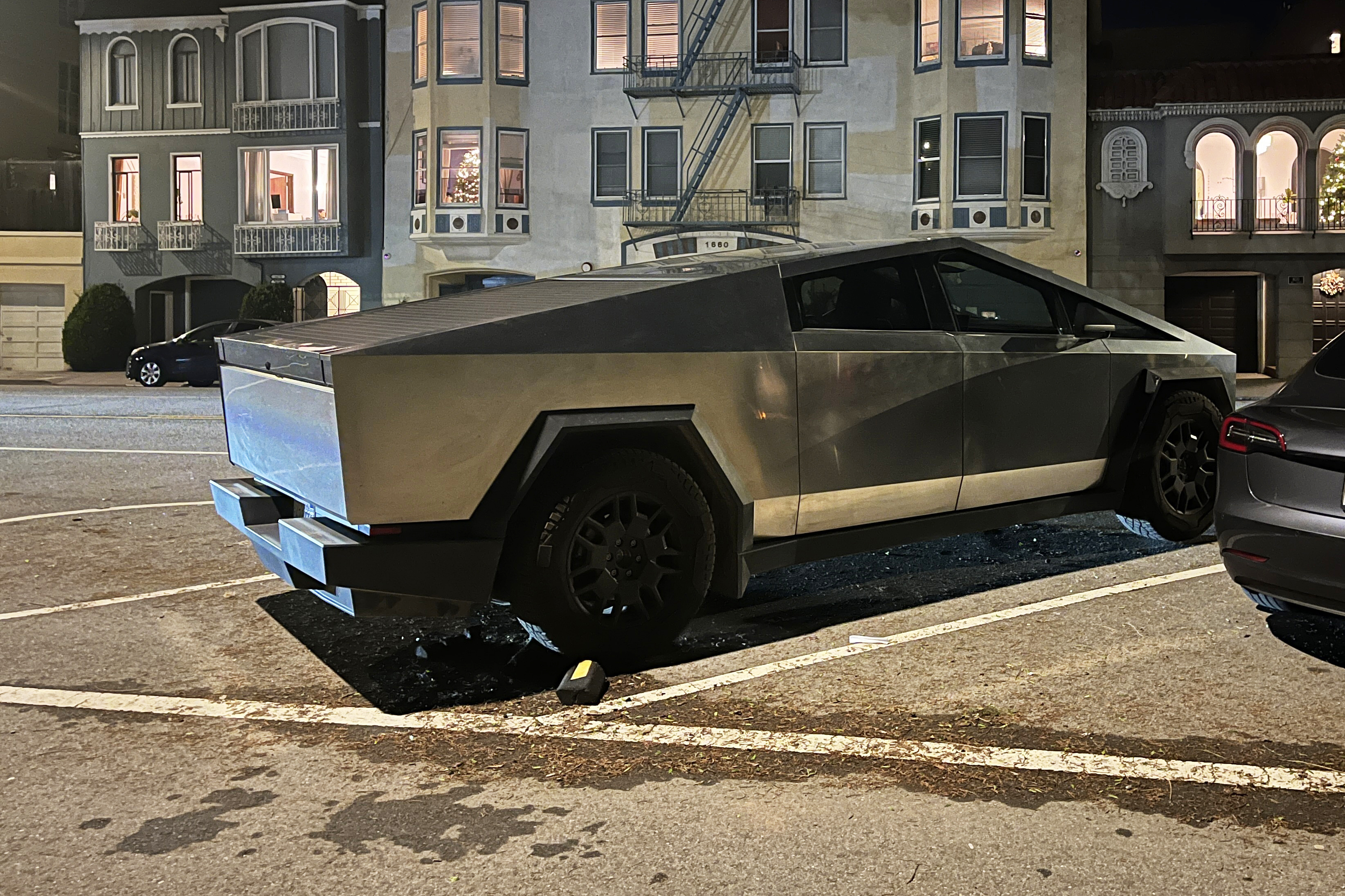 A futuristic-looking, angular vehicle parked on a city street at night, with traditional houses in the background.